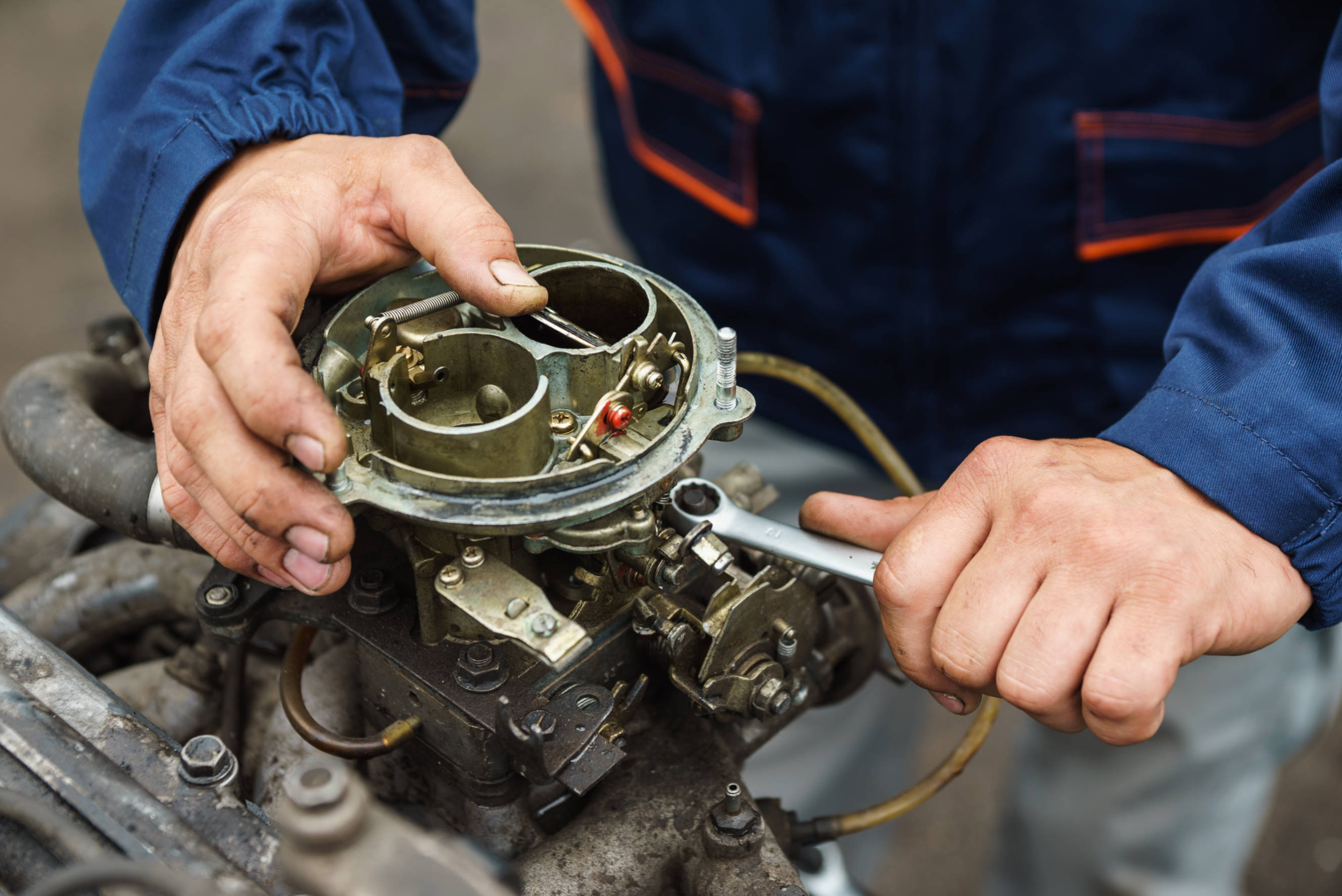 Mechanic performing carburetor tuning using a wrench to adjust the components of a car’s carburetor.