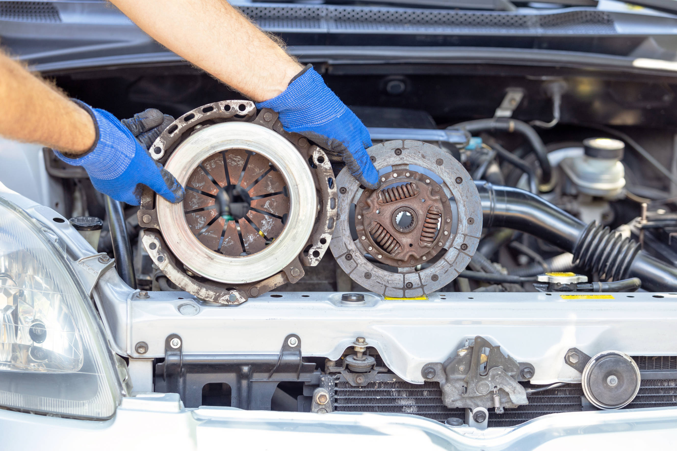 Mechanic holding car clutch parts while performing a clutch replacement in an open engine bay.