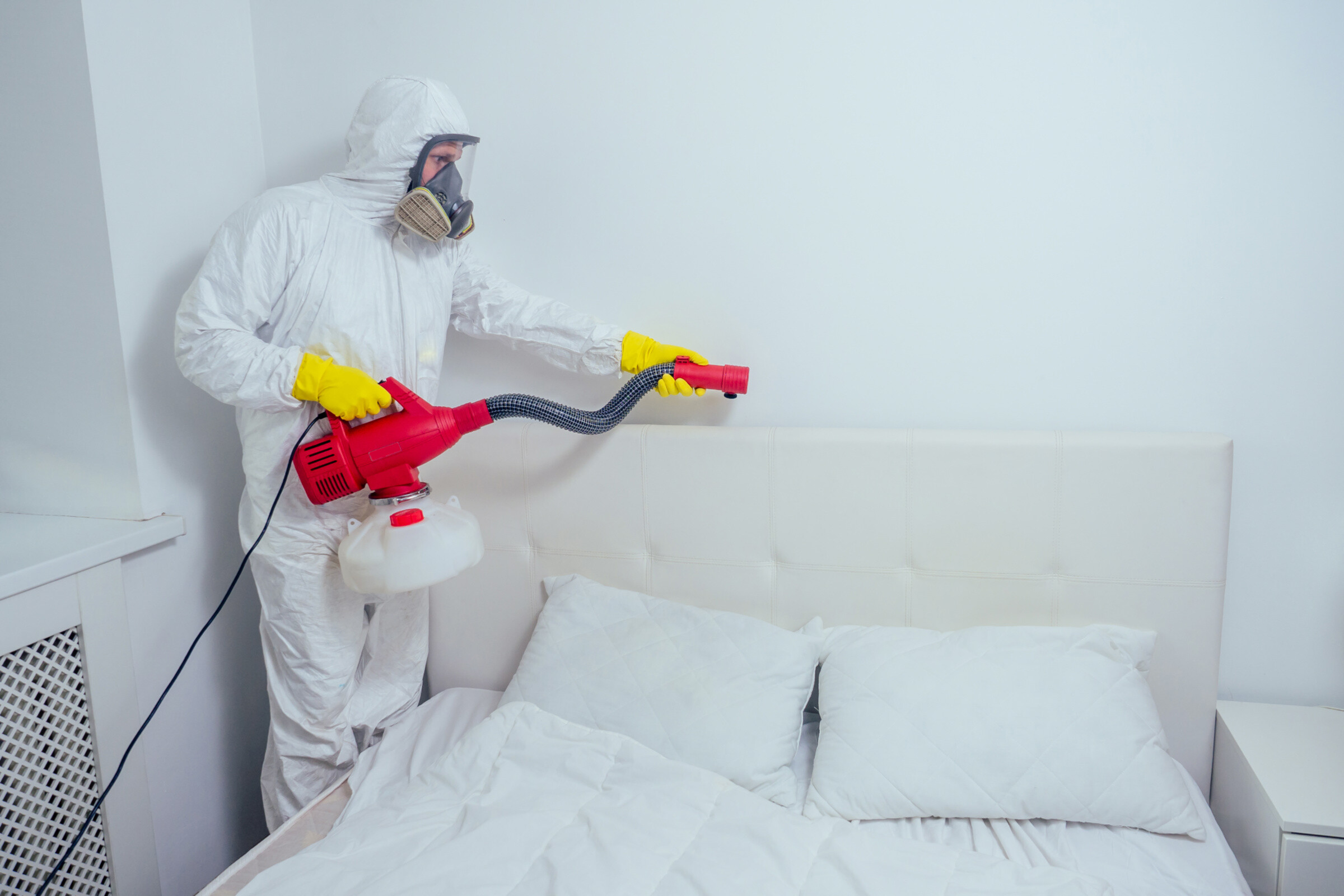 A pest control professional in a hazmat suit doing bed bug removal.