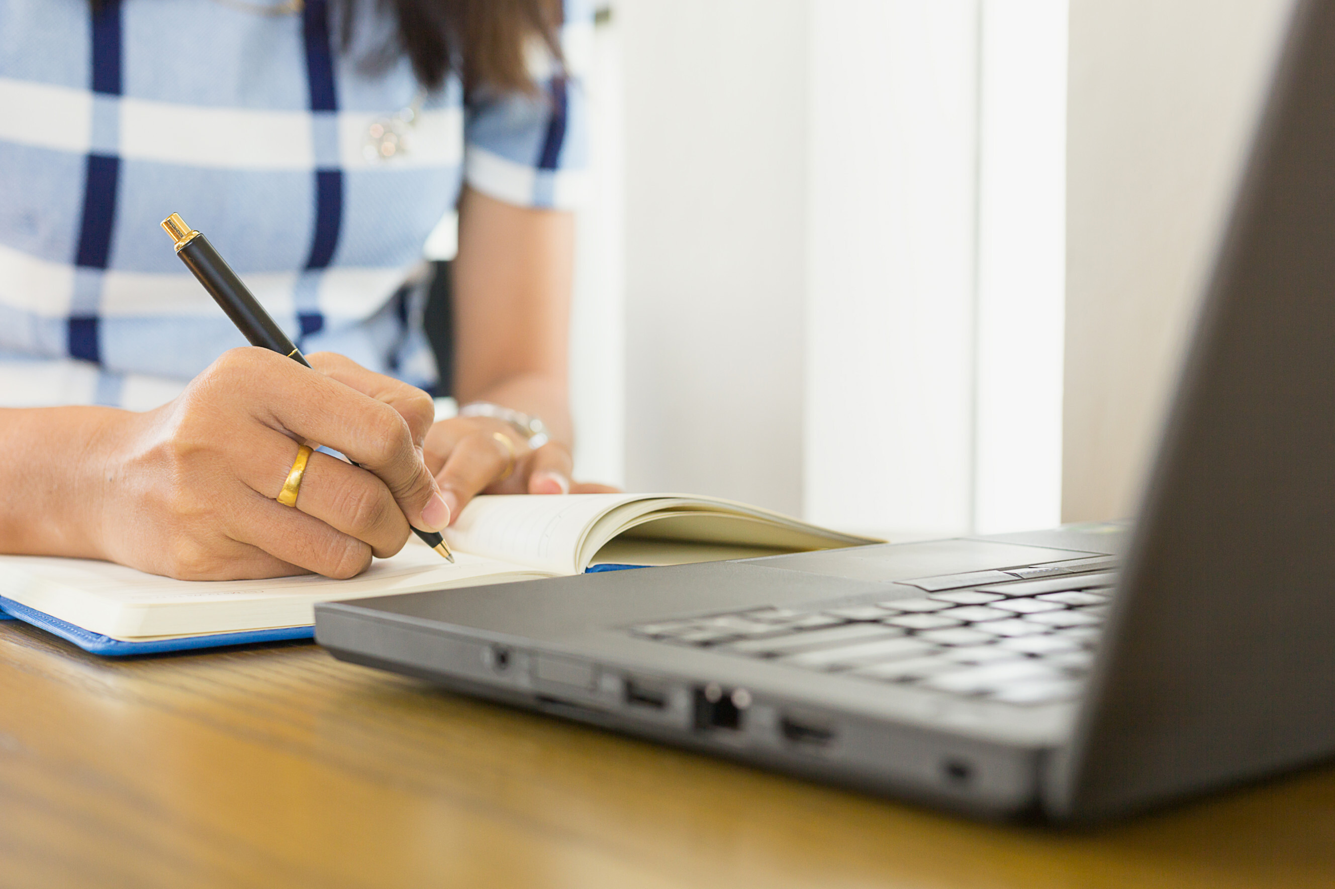 Person writing in a notebook with a laptop nearby, representing blog writing services.