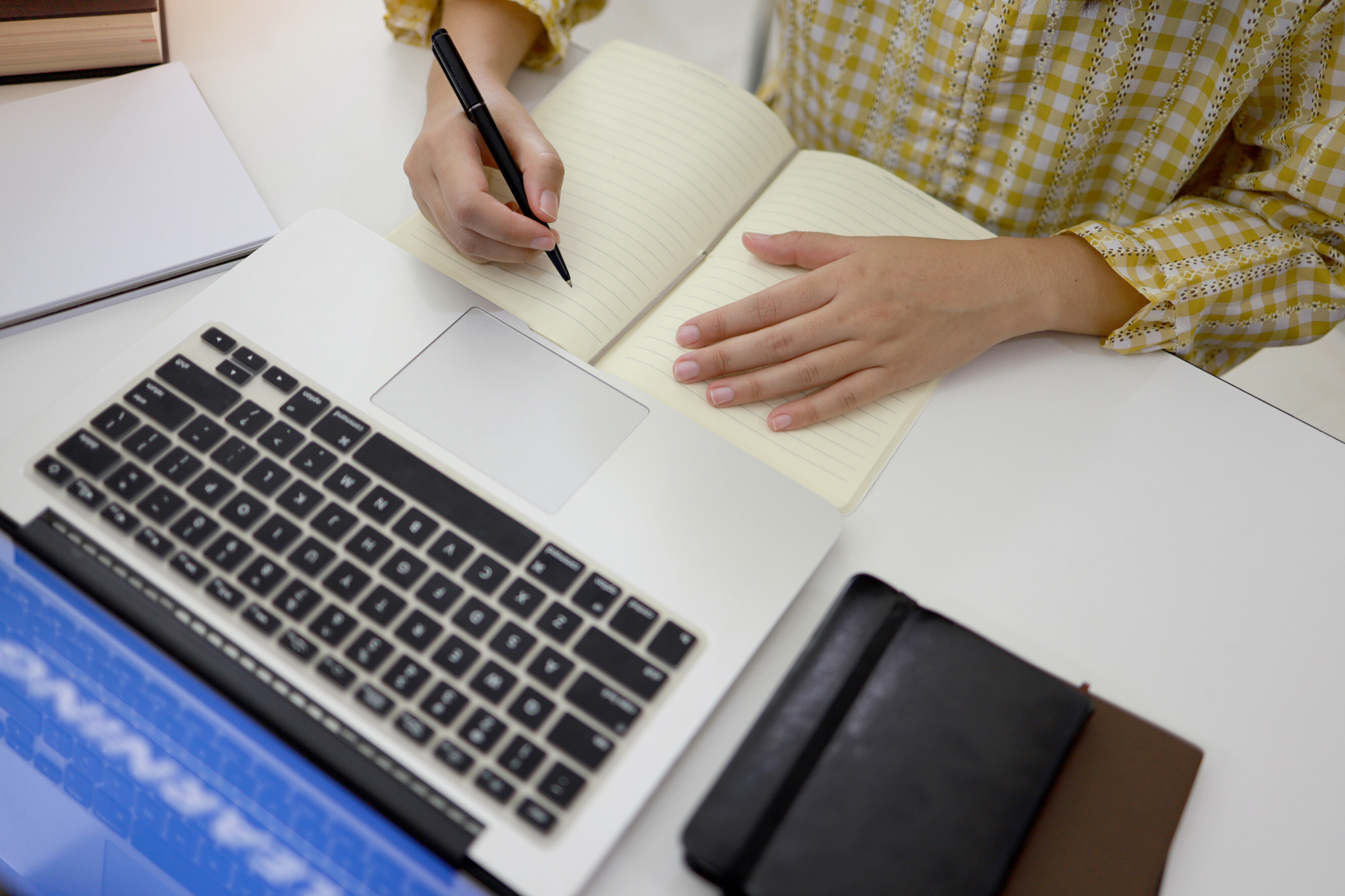 Person writing in a notebook beside a laptop, symbolizing case study writing services.