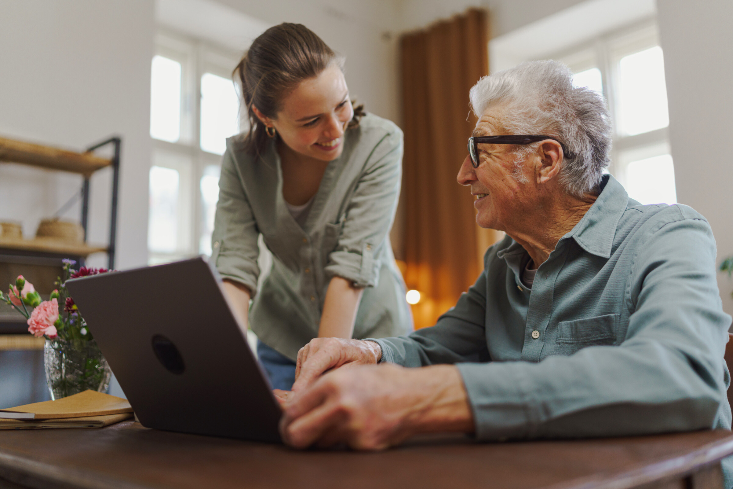 A computer expert training or teaching a senior citizen how to navigate their Macbook.