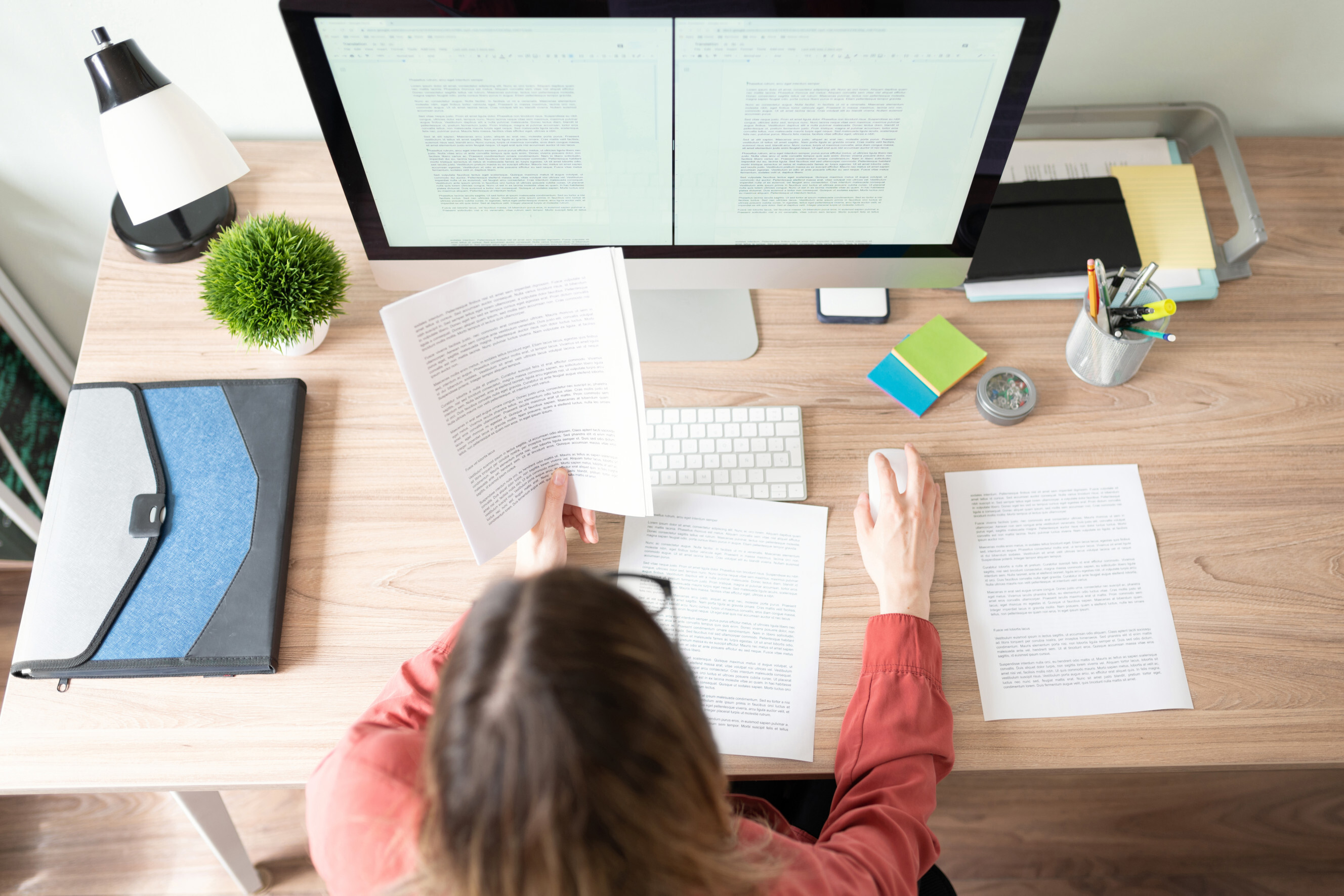 A person sitting on a desk, in front of a computer, reading a piece of paper symbolizing content creation.