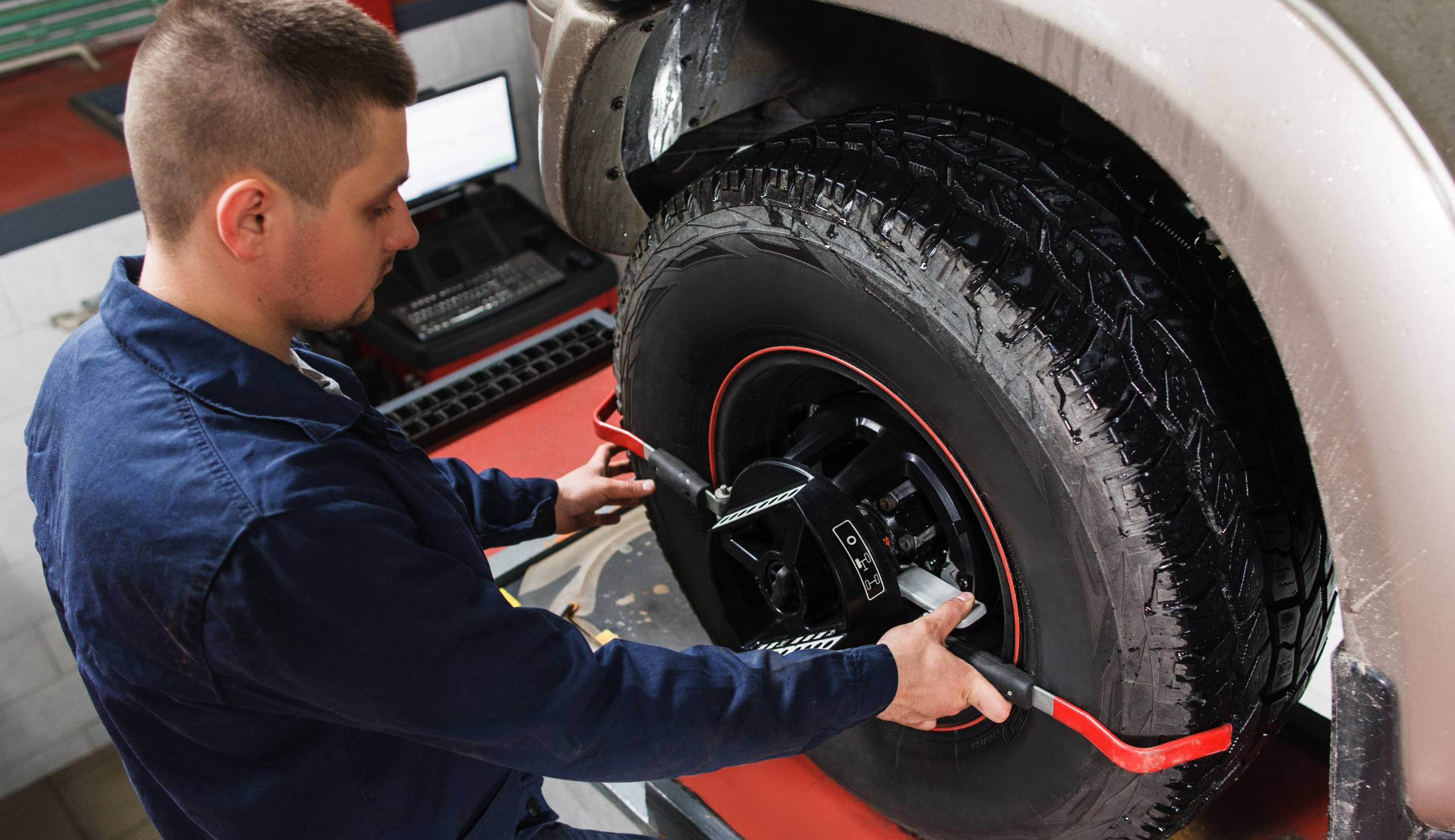 A mechanic performing wheel alignment on a vehicle using special tools. 