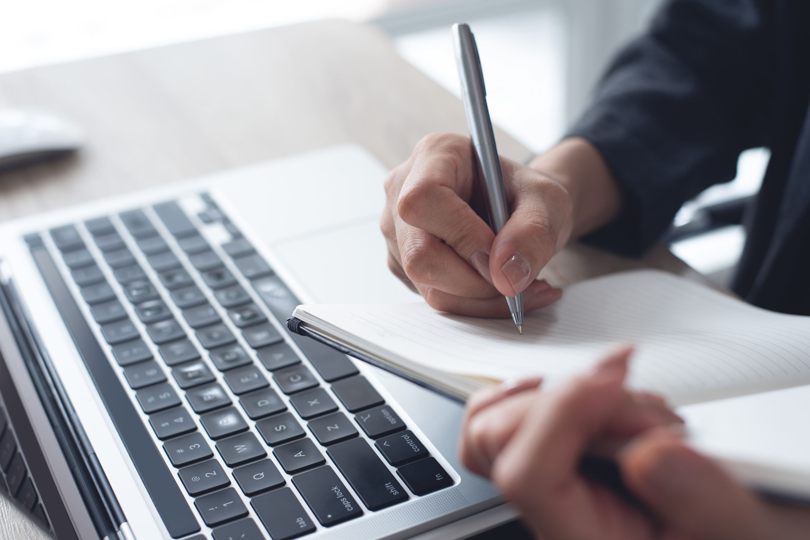 A woman holding a pen and writing in a notebook representing ghostwriting.