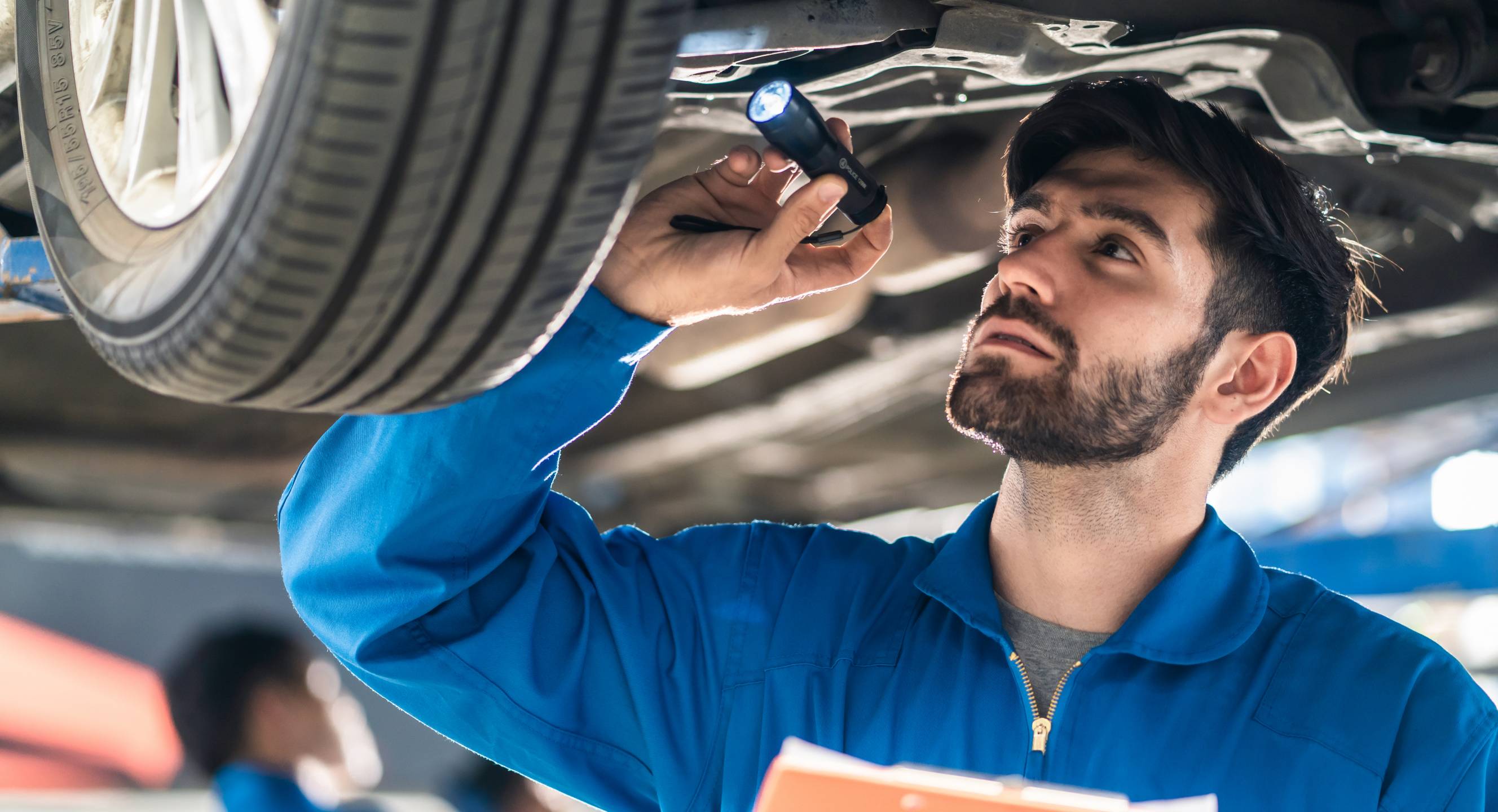 A mechanic inspects a car's wheel tracking and alignment under a vehicle lift.