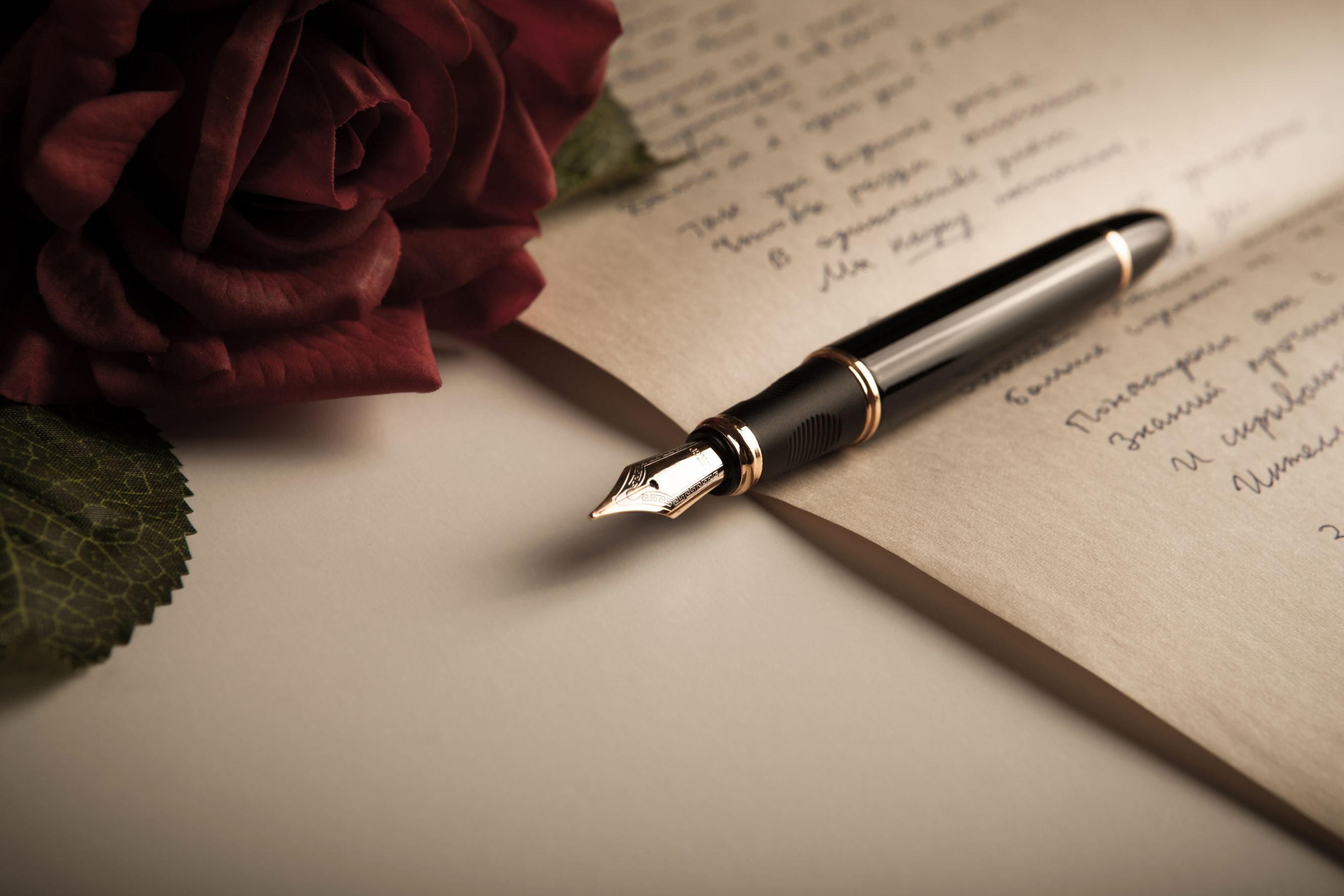 A fountain pen on text sheet paper with rose close-up symbolizing poetry writing.