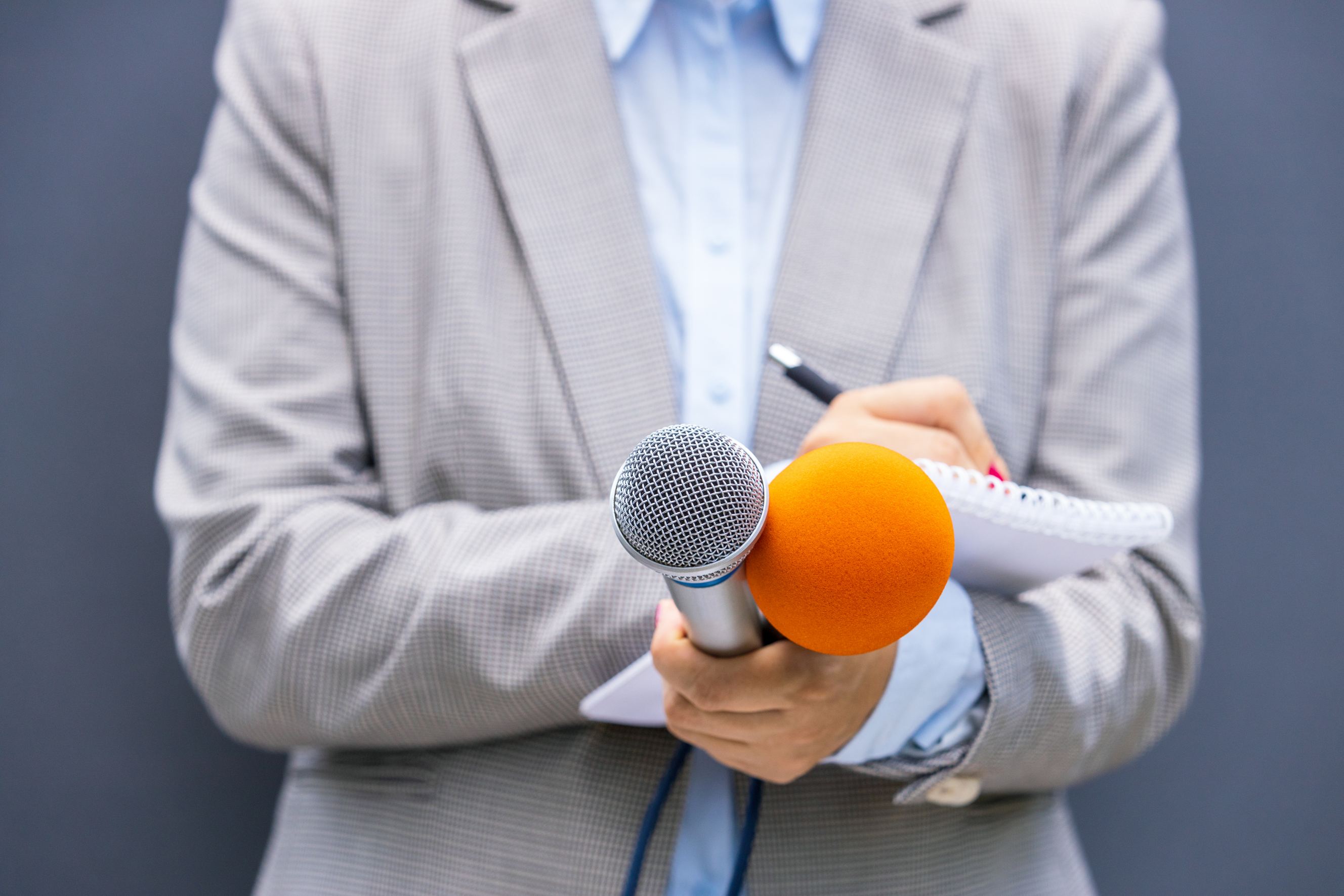 Female press release writer at a news conference, writing notes, holding a microphone.