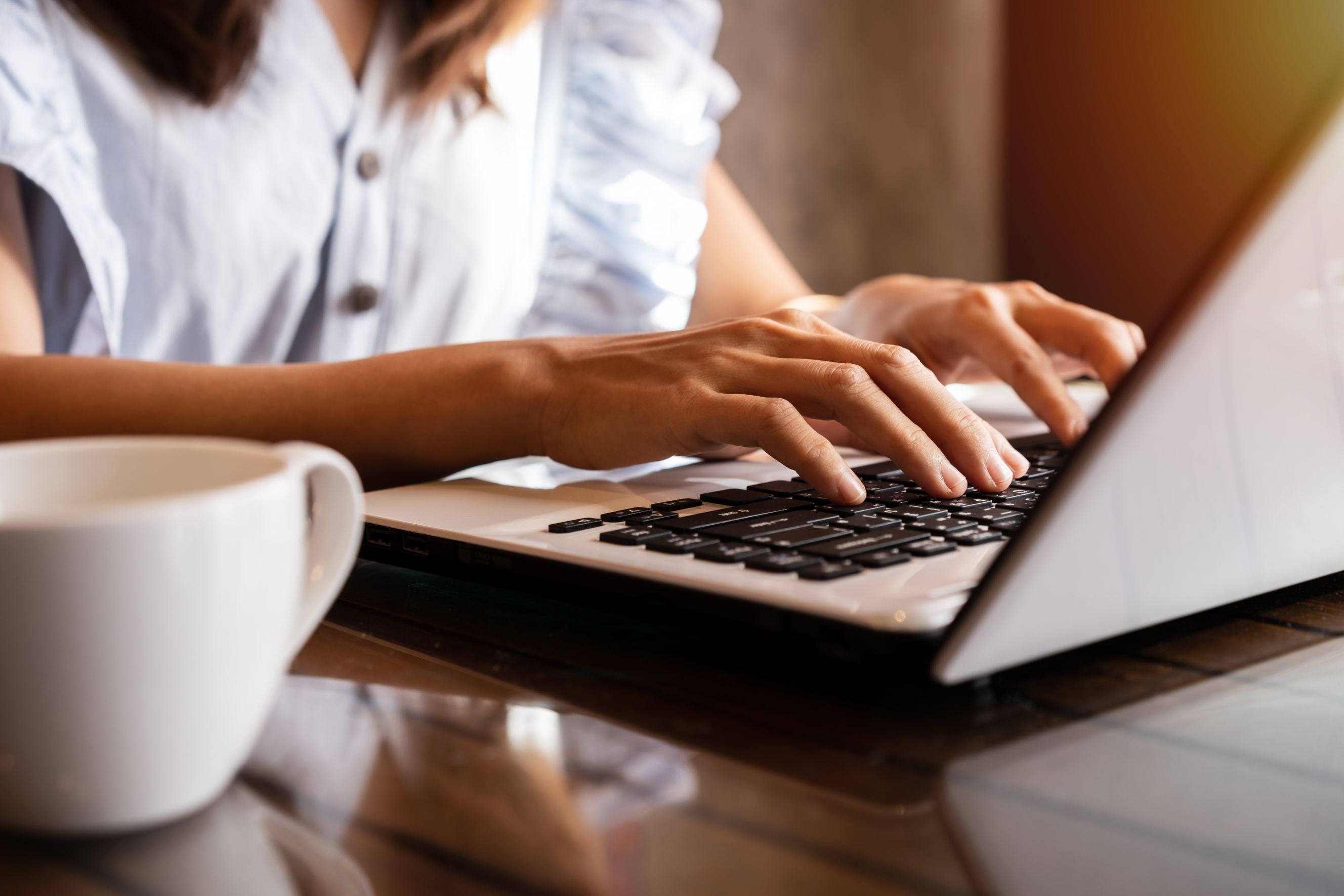 A young woman with a cup of coffee in a cafe using a laptop for her report writing.