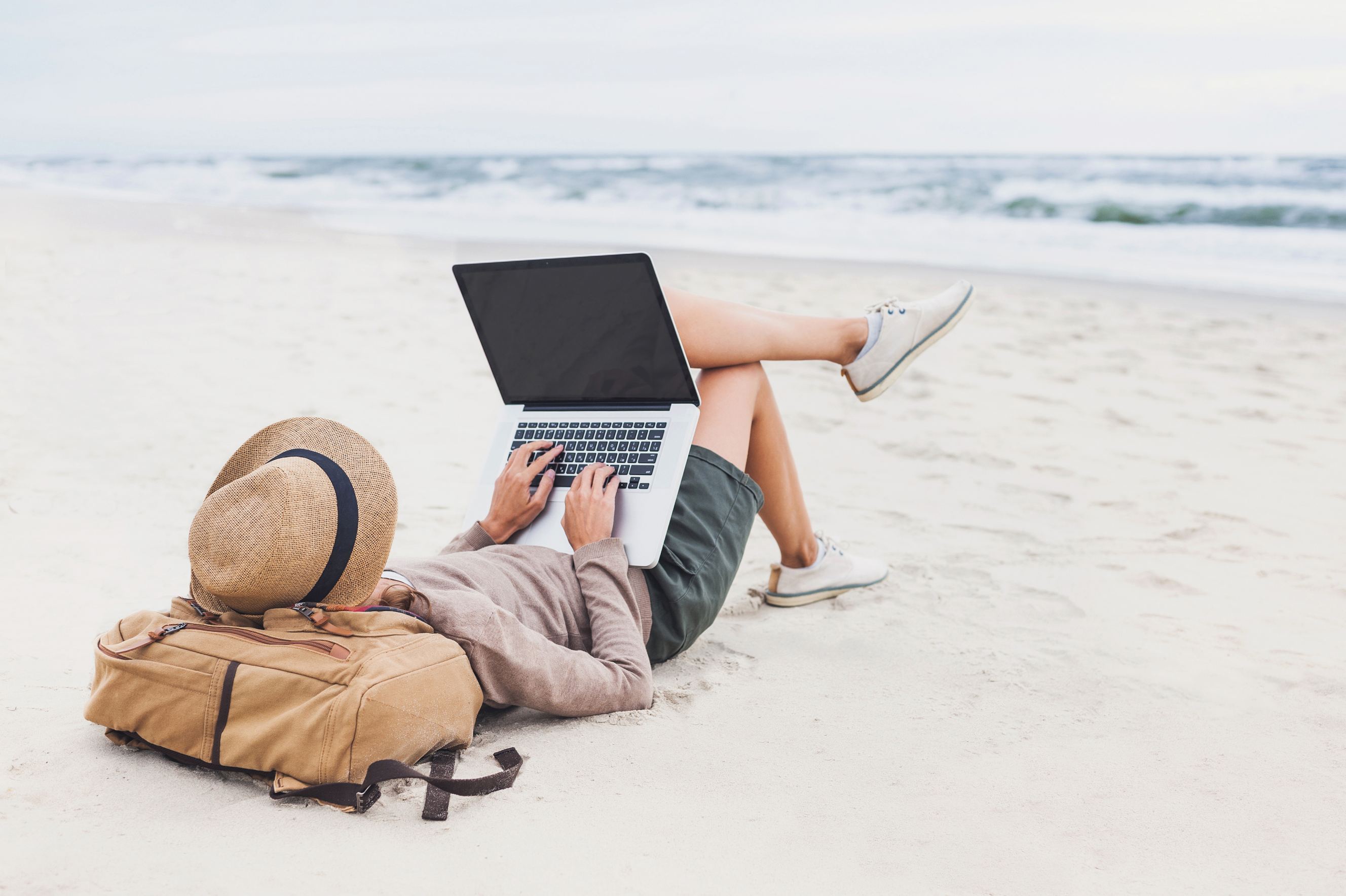 A lady travel writer using a laptop on a beach.