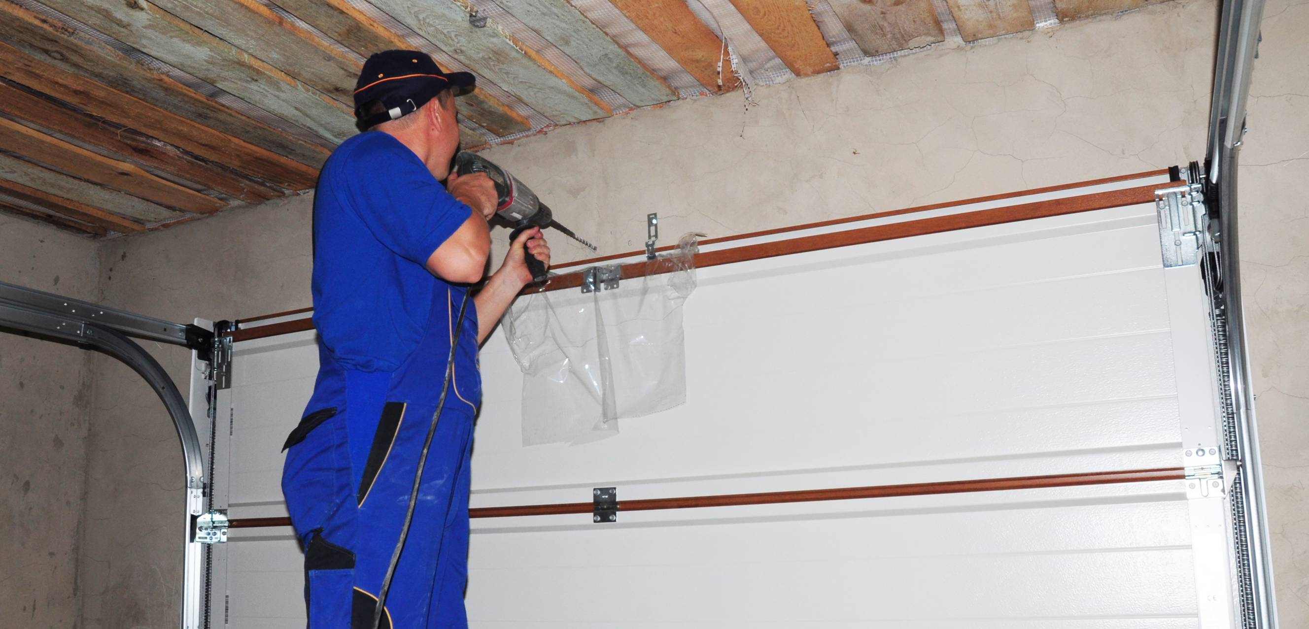 A contractor using power tools and helping with garage door installation for a home.