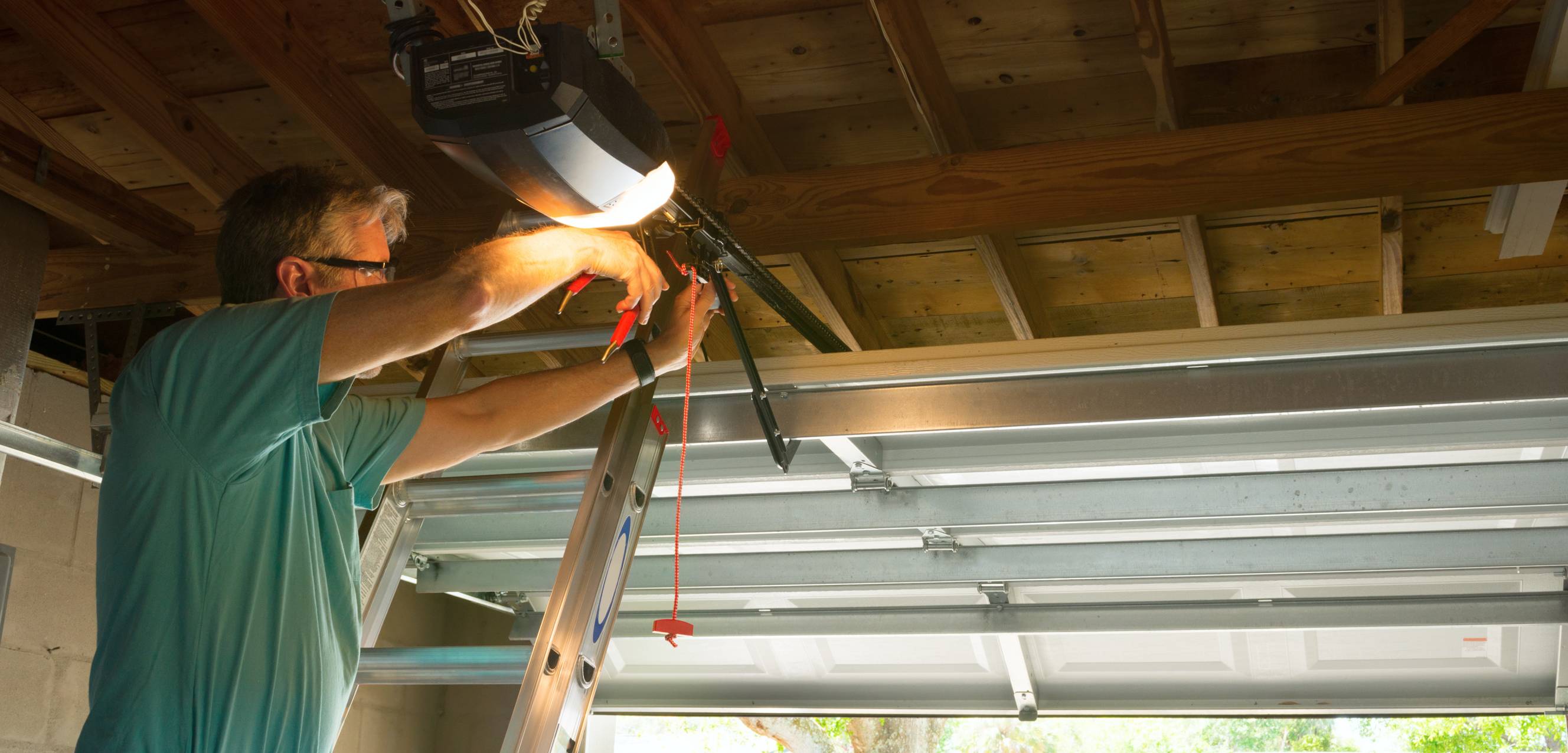 A handyman using a power tool and ladder for garage door repairs.