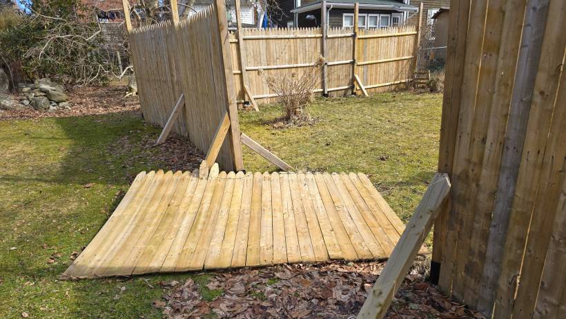 A pile of wooden planks and boards laid out in a backyard, presumably to be used for constructing or repairing a wooden fence - fencing cost