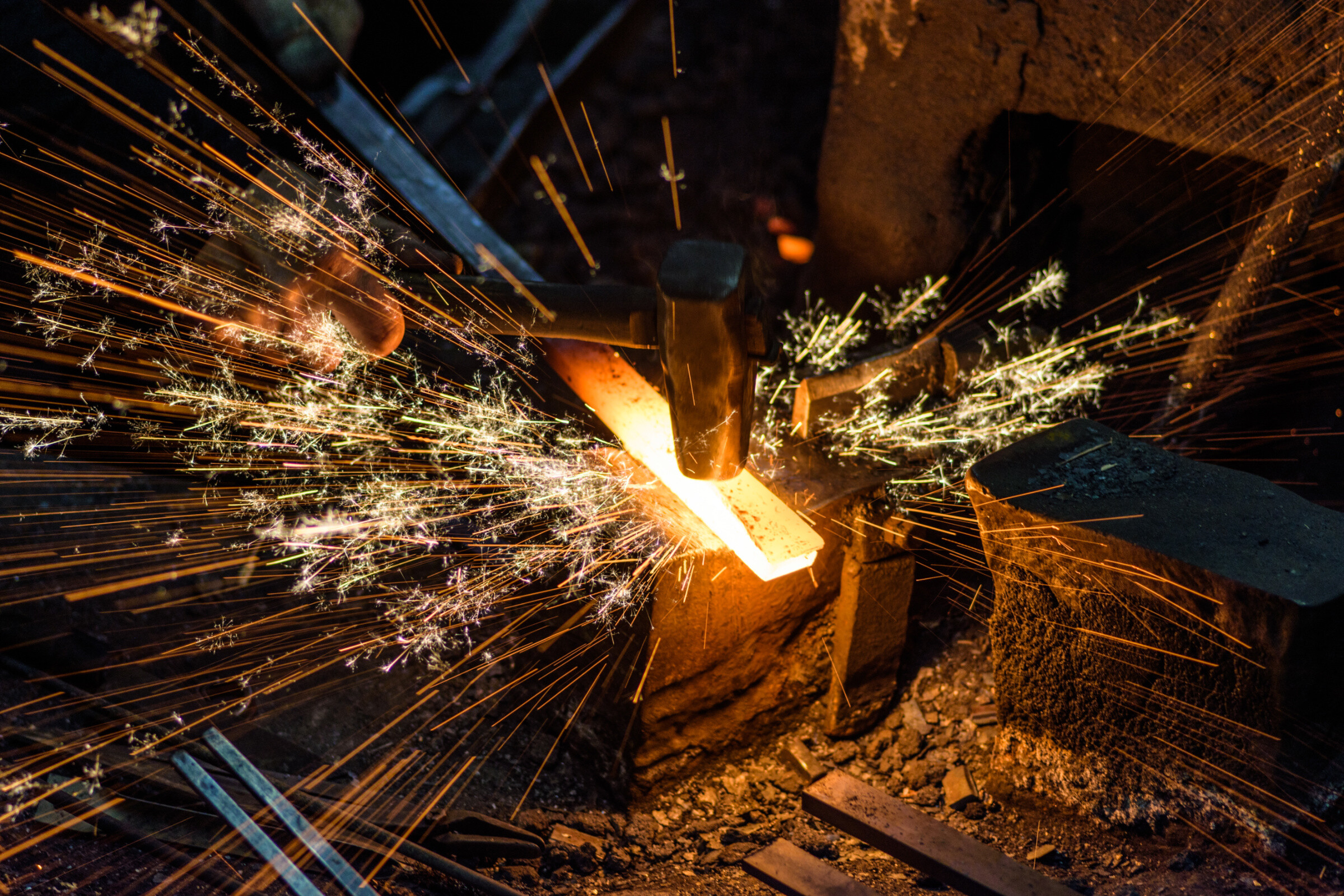 Top view of sparks flying as a blacksmith hammers a hot iron ingot.