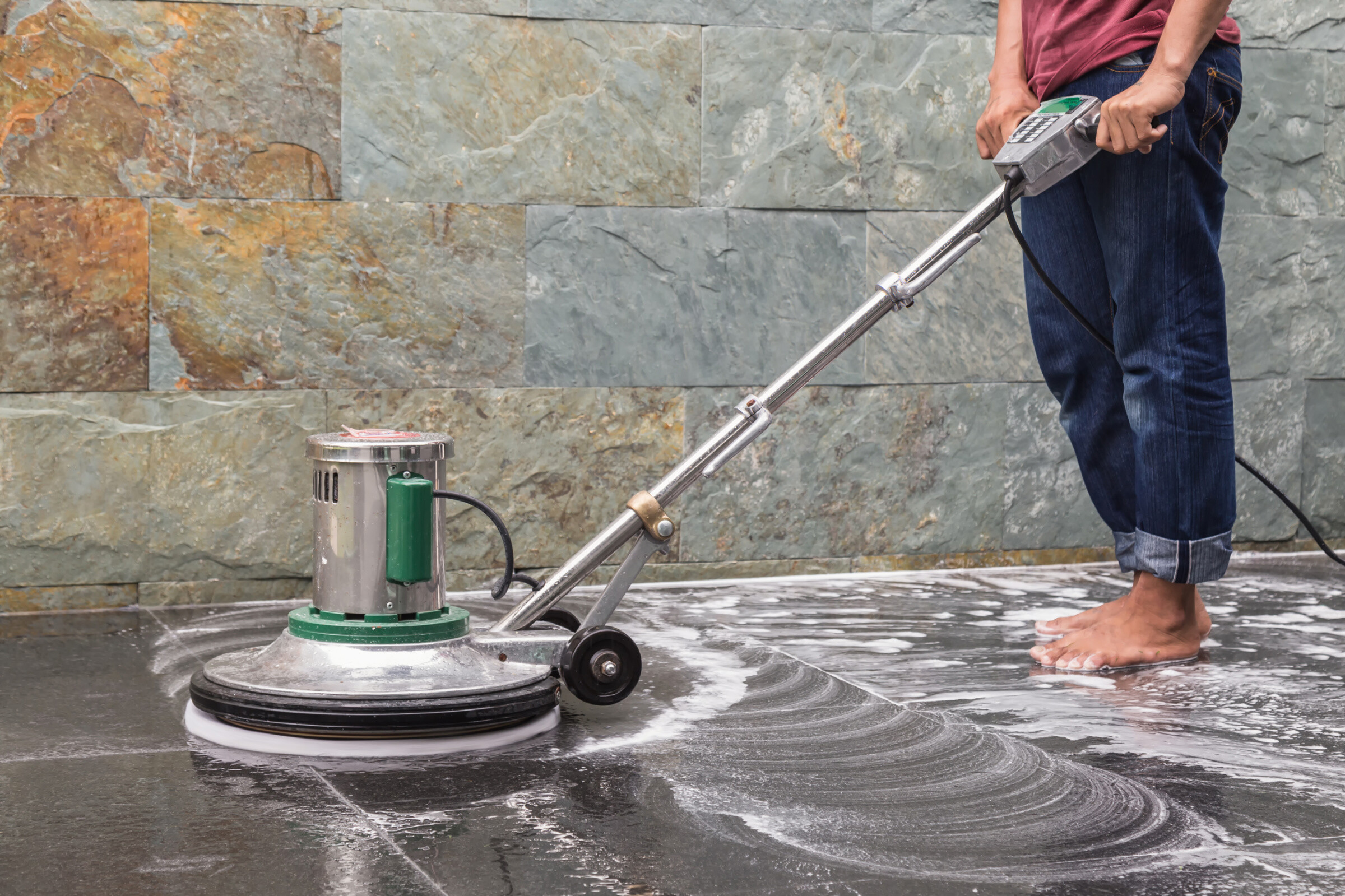 A barefoot worker cleaning and polishing concrete floor tiles.