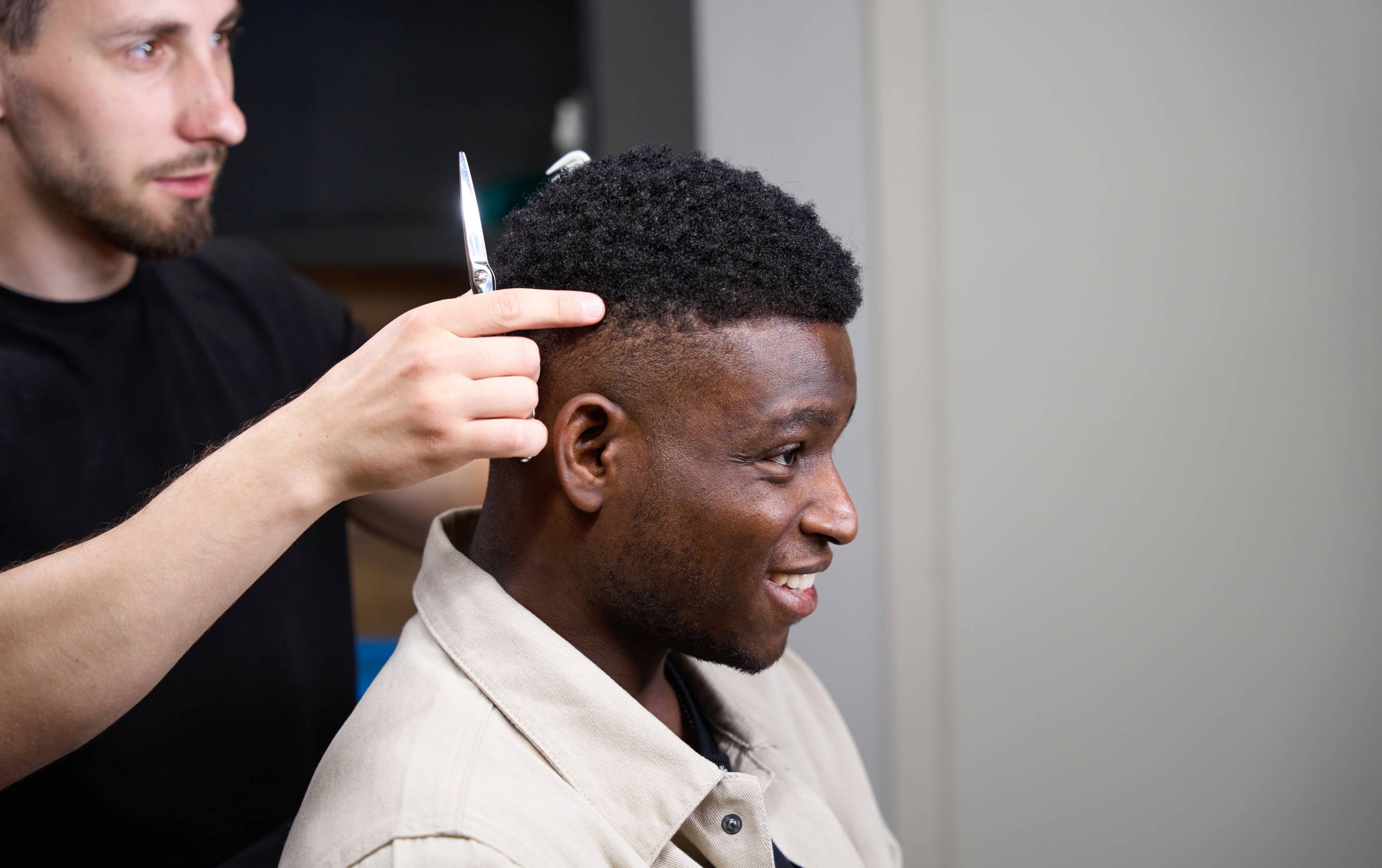 An afro barber giving a haircut to a client with short, curly hair.