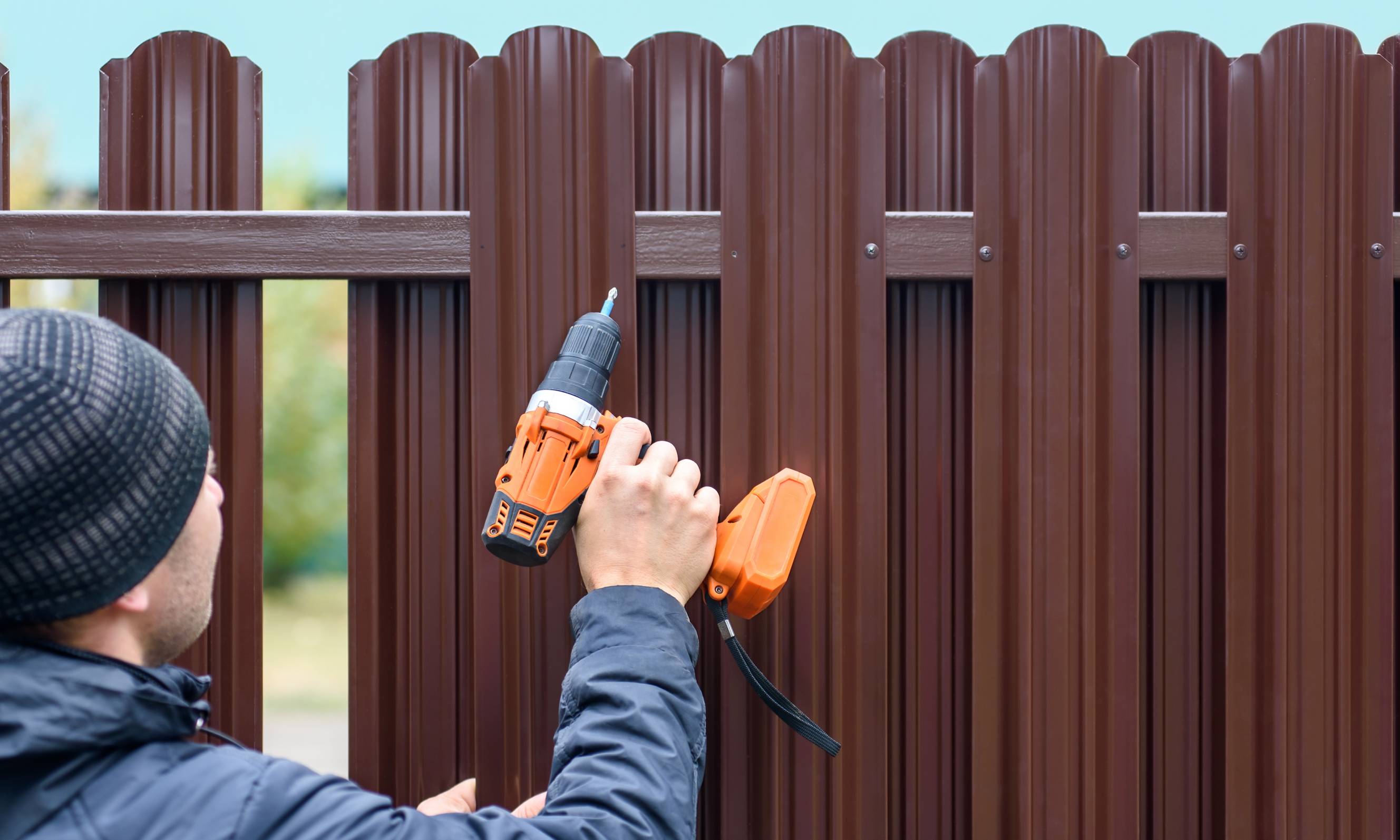 A fencing contractor installing a brown aluminium fence using a screwdriver.