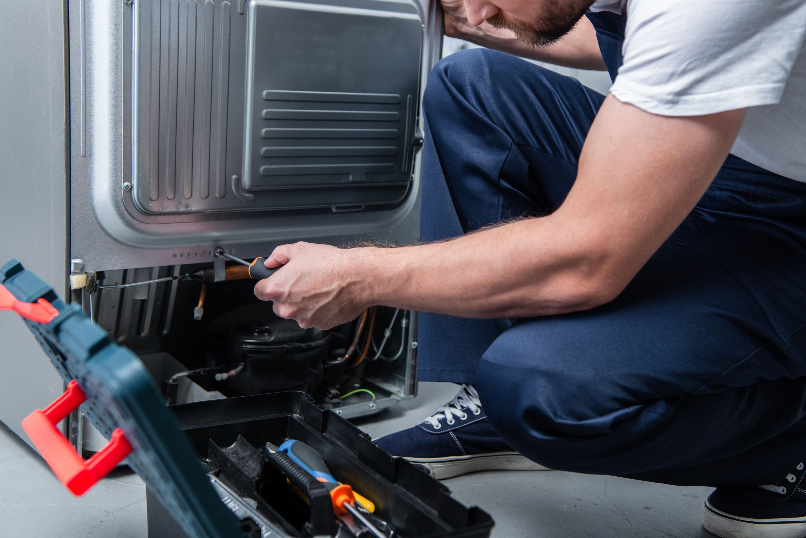 Partial view of repairman in working overall fixing refrigerator representing Frigidaire repair.