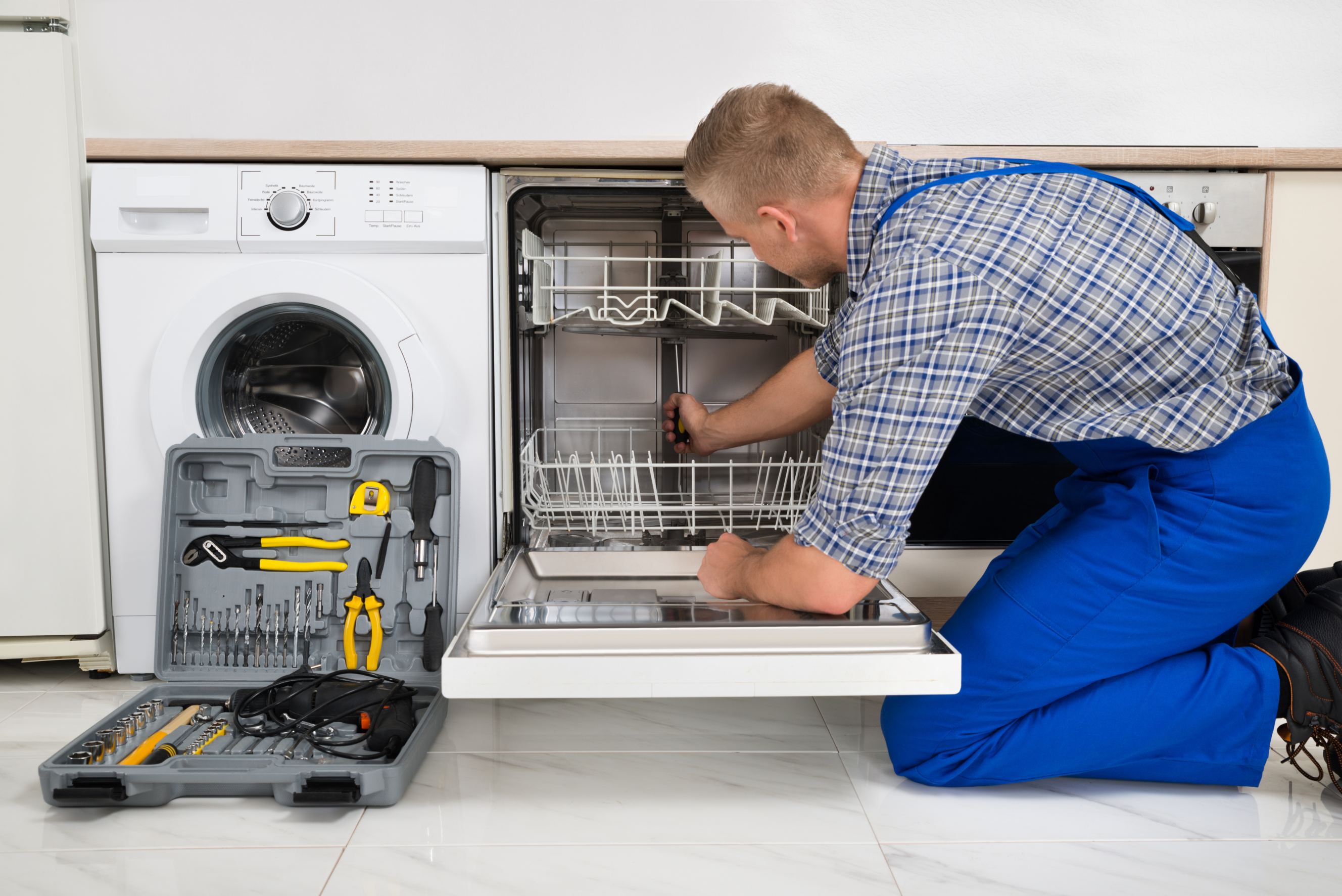 A young man in overalls with a toolbox doing GE dishwasher repair.