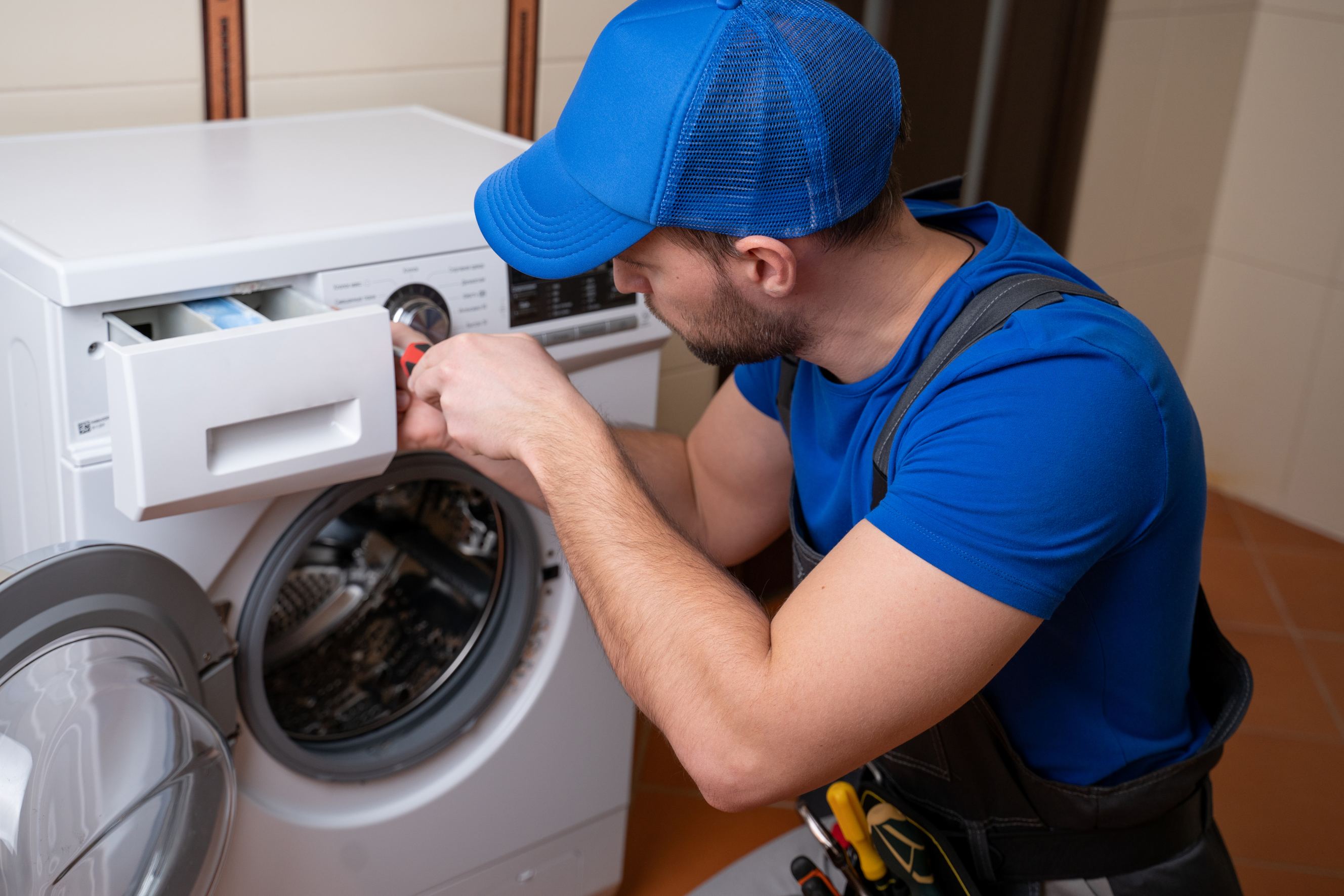 Worker repairing washing machine in laundry room representing Maytag appliance repair.