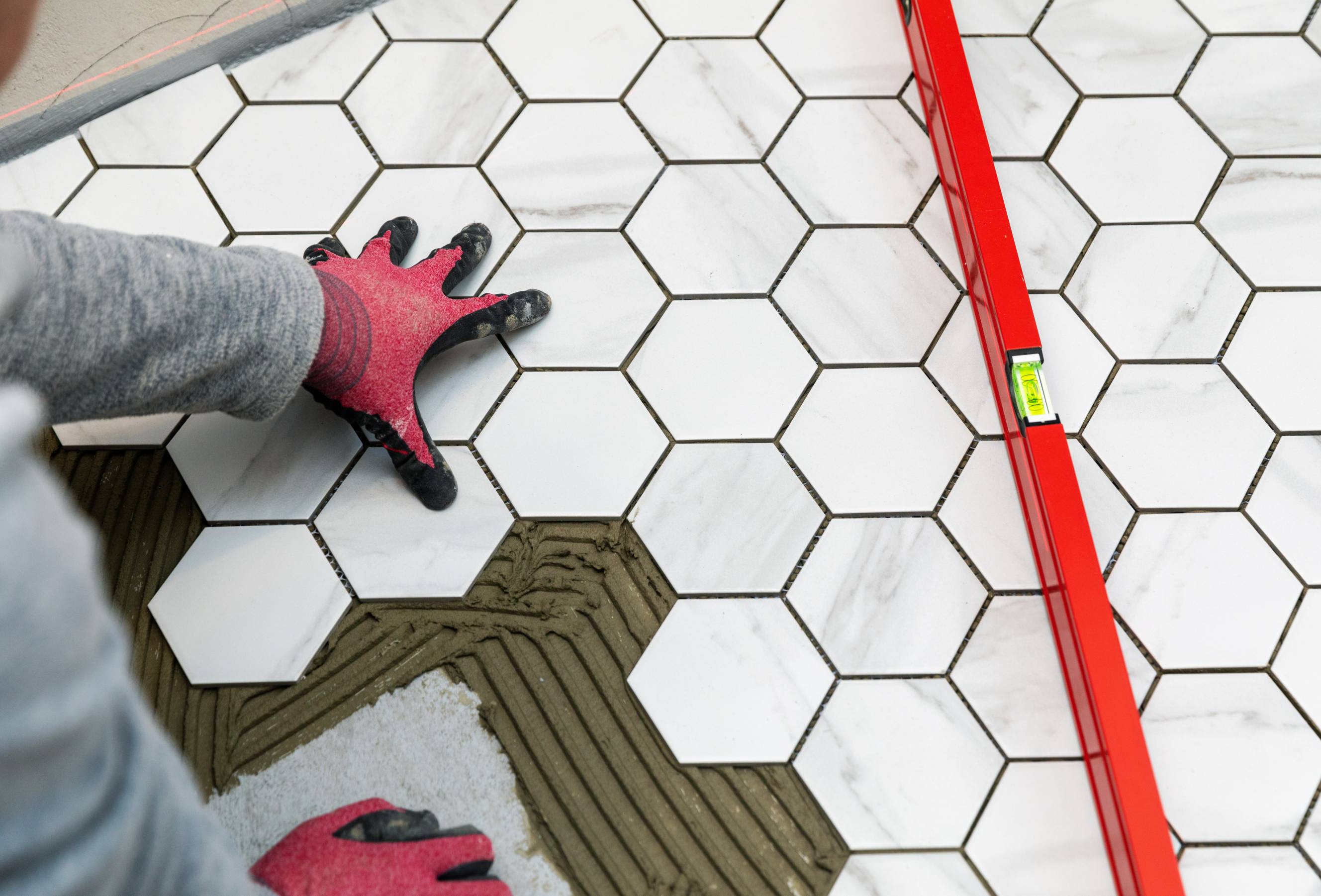 A professional contractor installing hexagon-shaped bathroom floor tiles. 