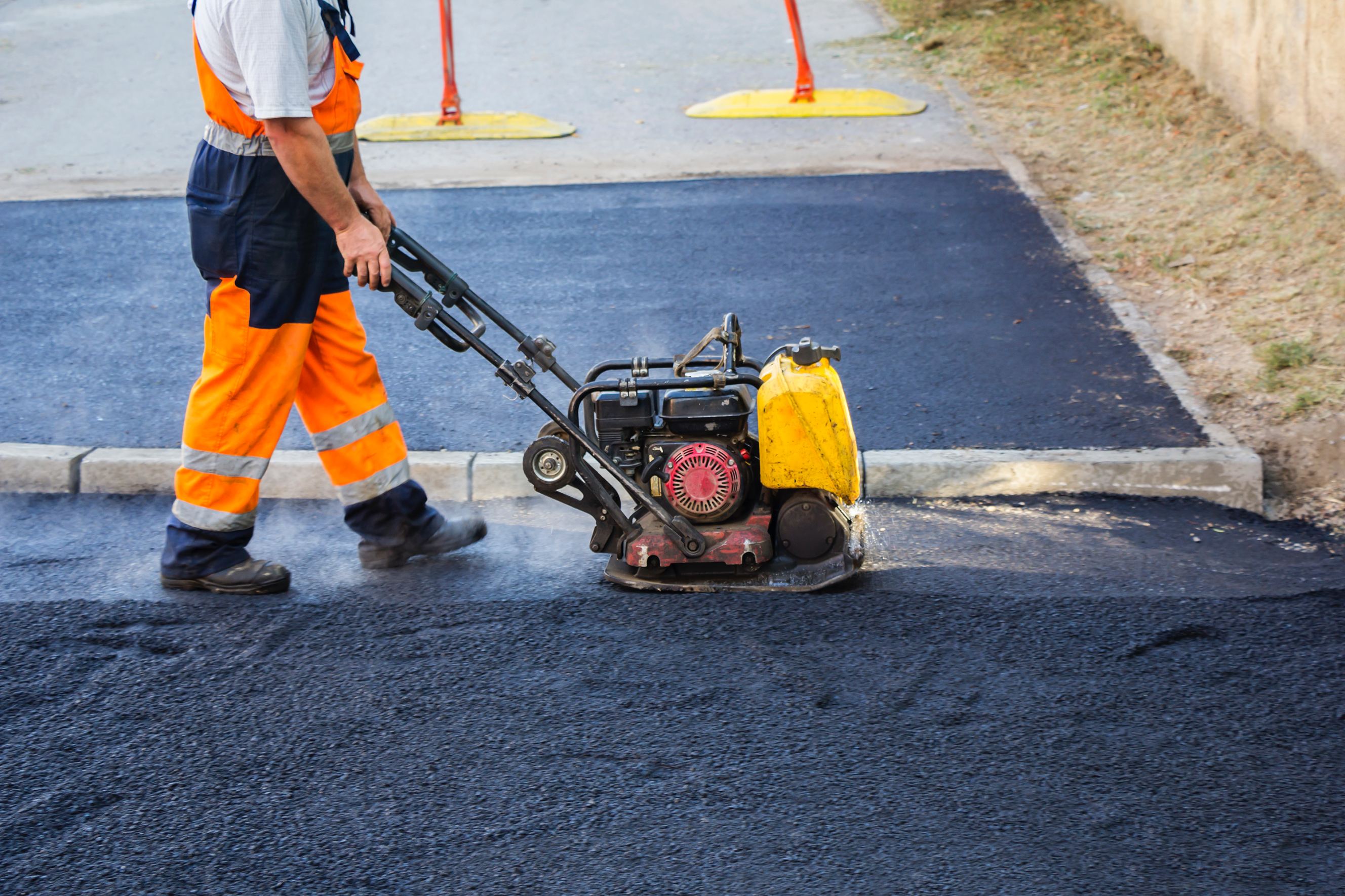 A worker using a vibratory plate compactor for asphalt repair.