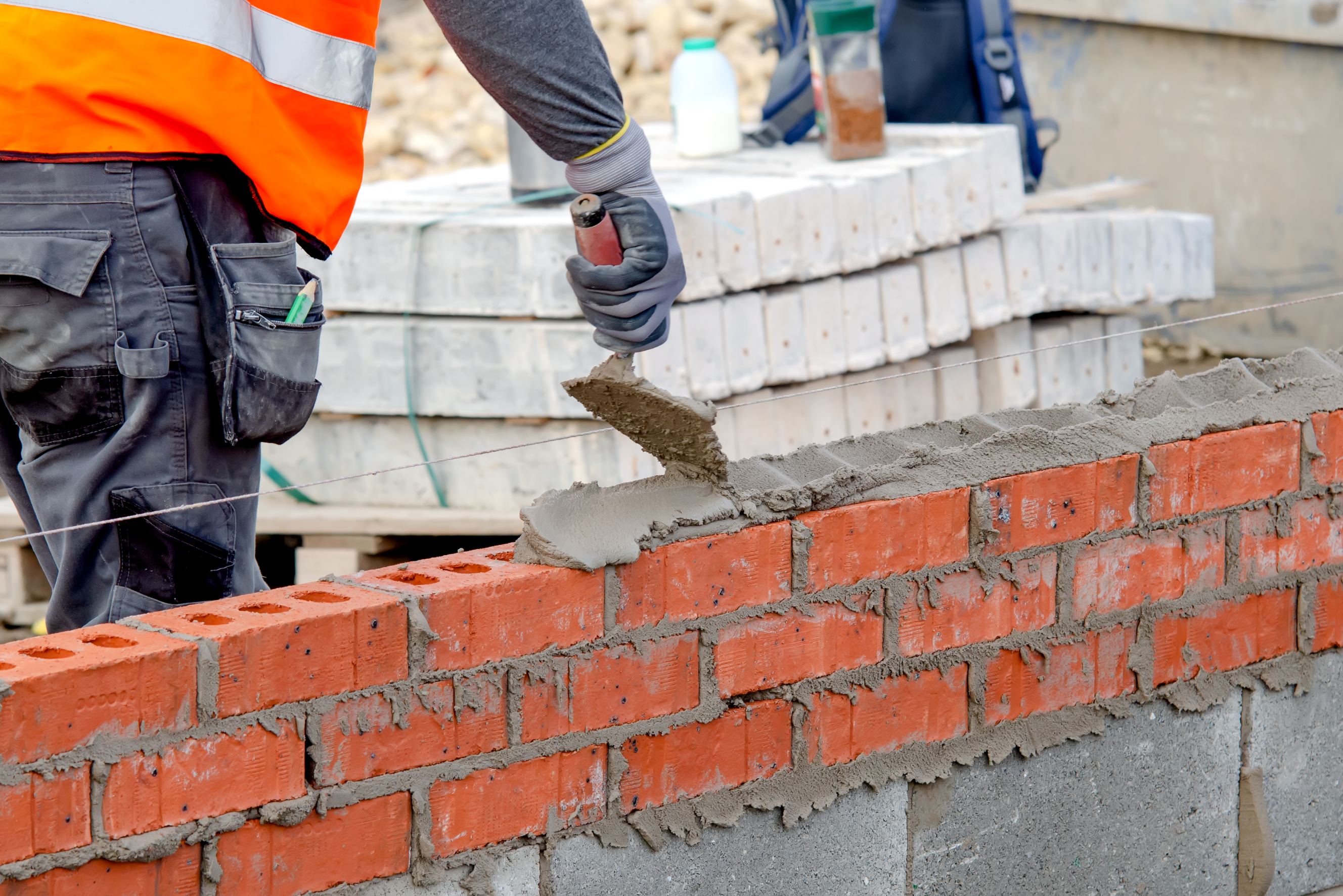 A mason is laying bricks on mortar on a new residential house construction site.