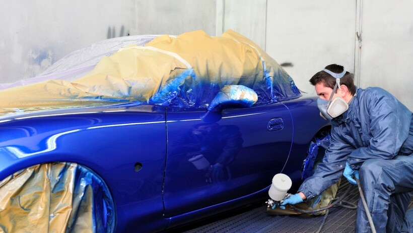 Car wrap vs paint - A technician painting a blue car in a workshop