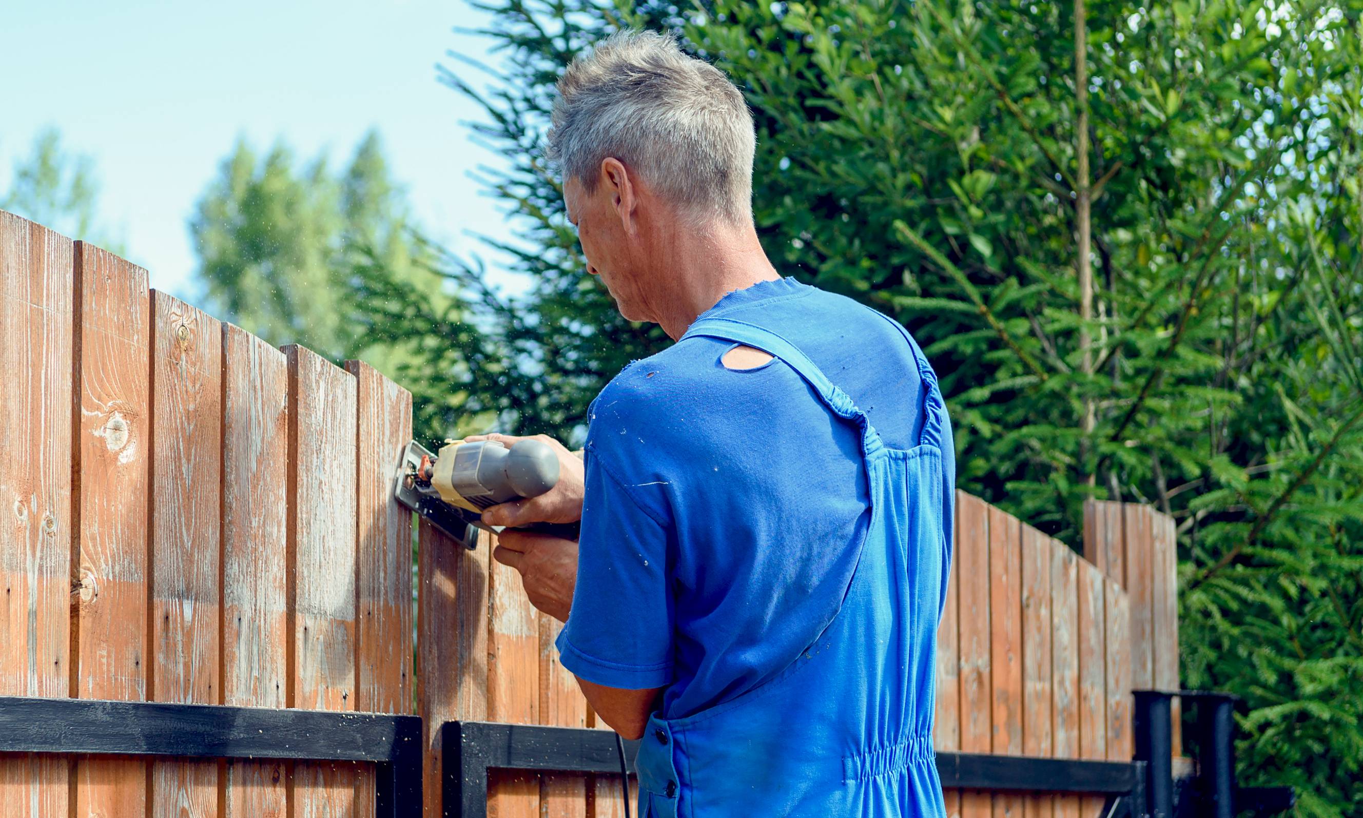 A fencing contractor using a jigsaw to align wooden panels as part of a fence repair service.