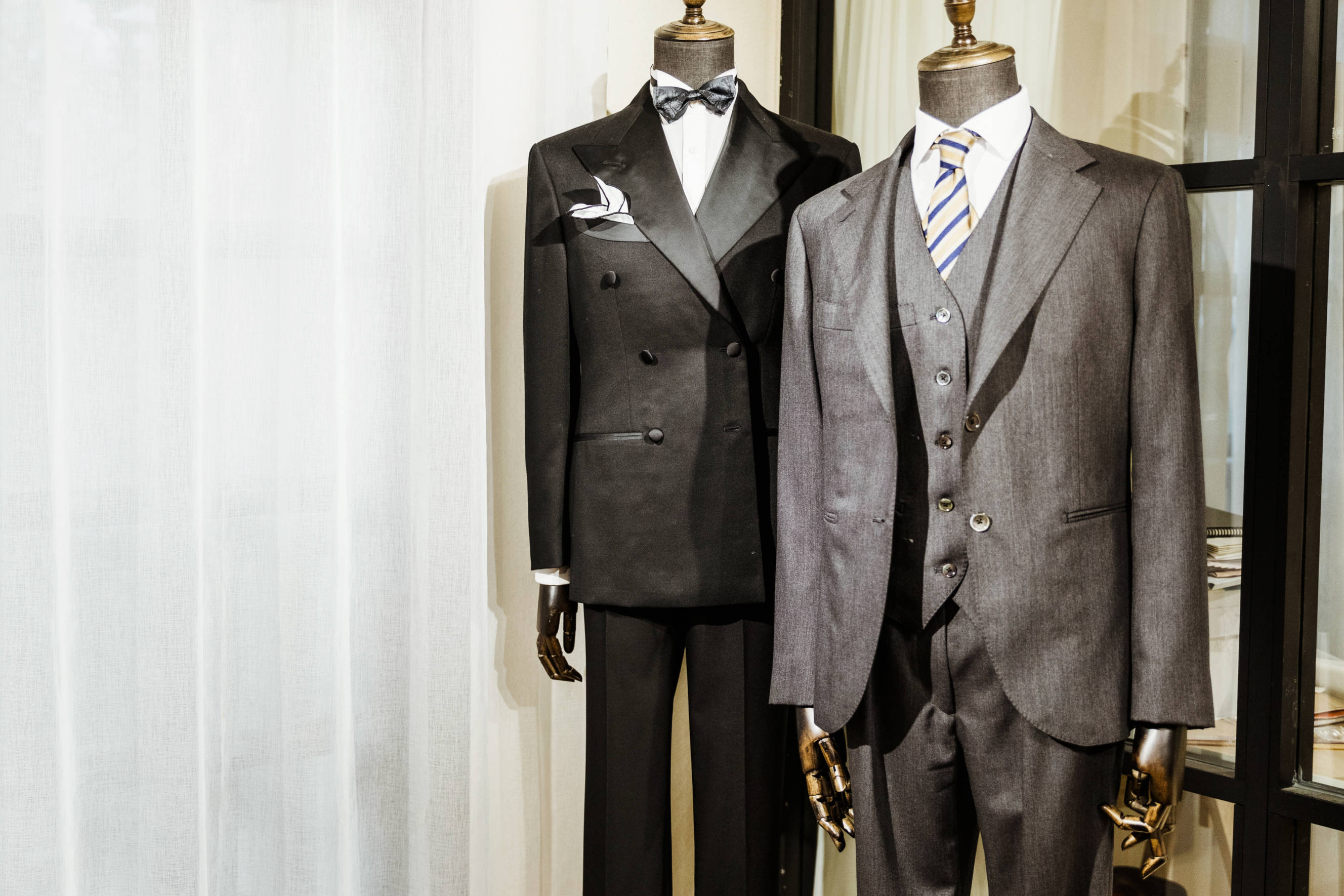 Double-breasted black suit with bow tie alongside single-breasted gray suit with striped tie, showcasing a comparison of double-breasted vs. single-breasted suits on mannequins.