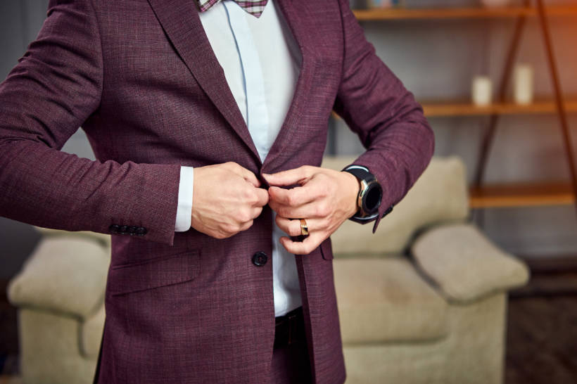 double breasted vs single breasted - man buttoning a single-breasted burgundy suit jacket, highlighting the style flexibility of the suit 