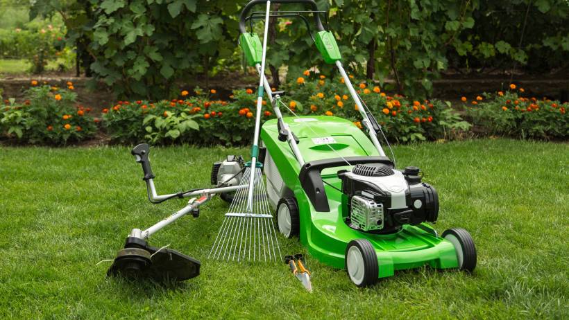 A modern, green-coloured lawn mower with other equipment in the garden. - lawn mowing cost