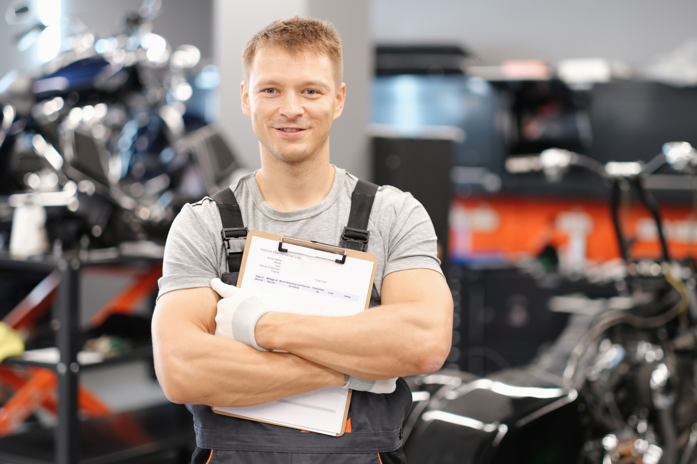 Handsome motorcycle mechanic posing in motorcycle service and holding documents in hands.