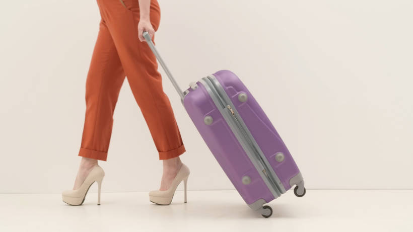 Chinos vs Khakis - Woman in formal chinos and high heels pulling a purple suitcase