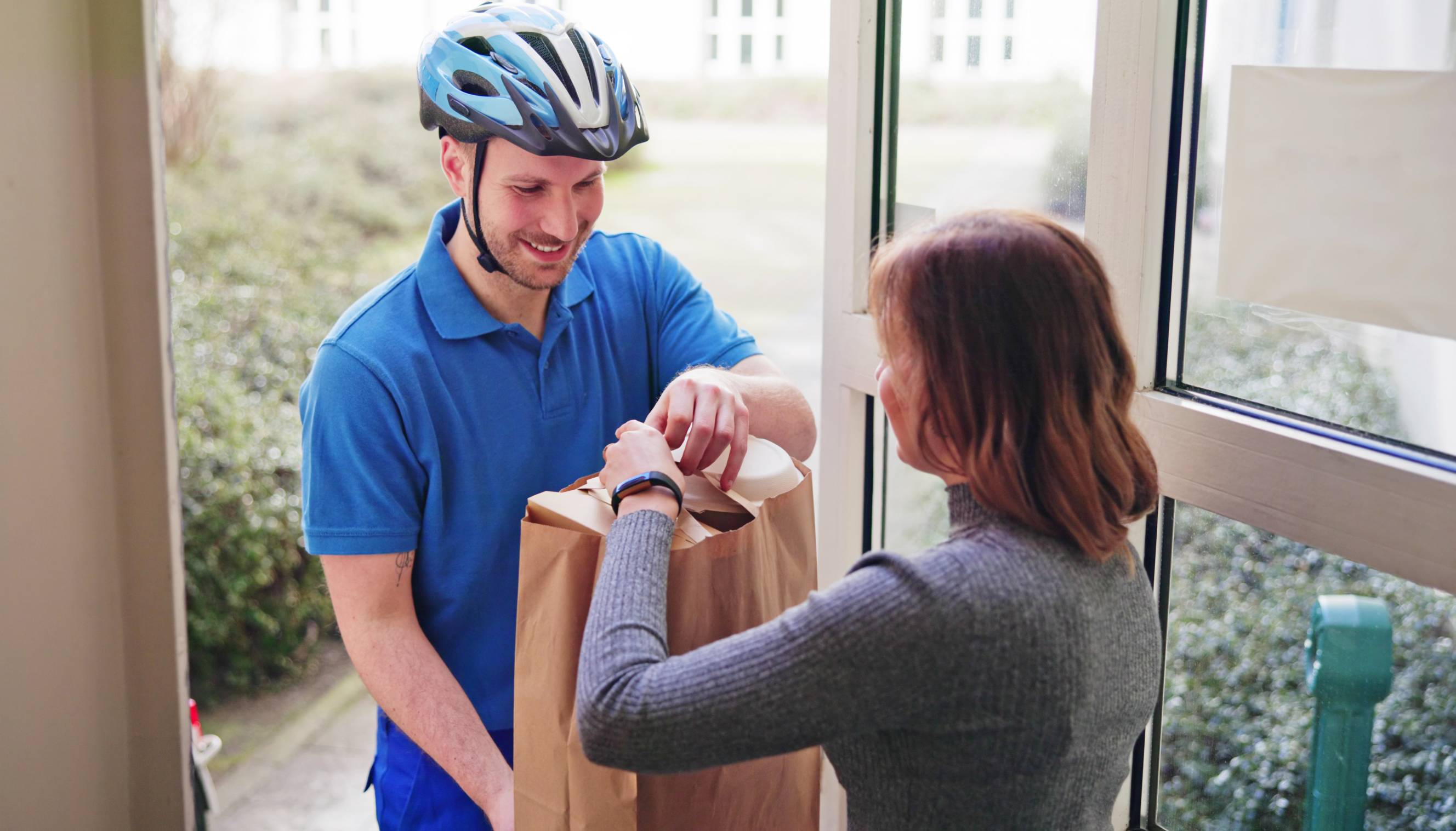 A delivery person handing a paper bag to a woman who ordered Ben and Jerry's delivery service.