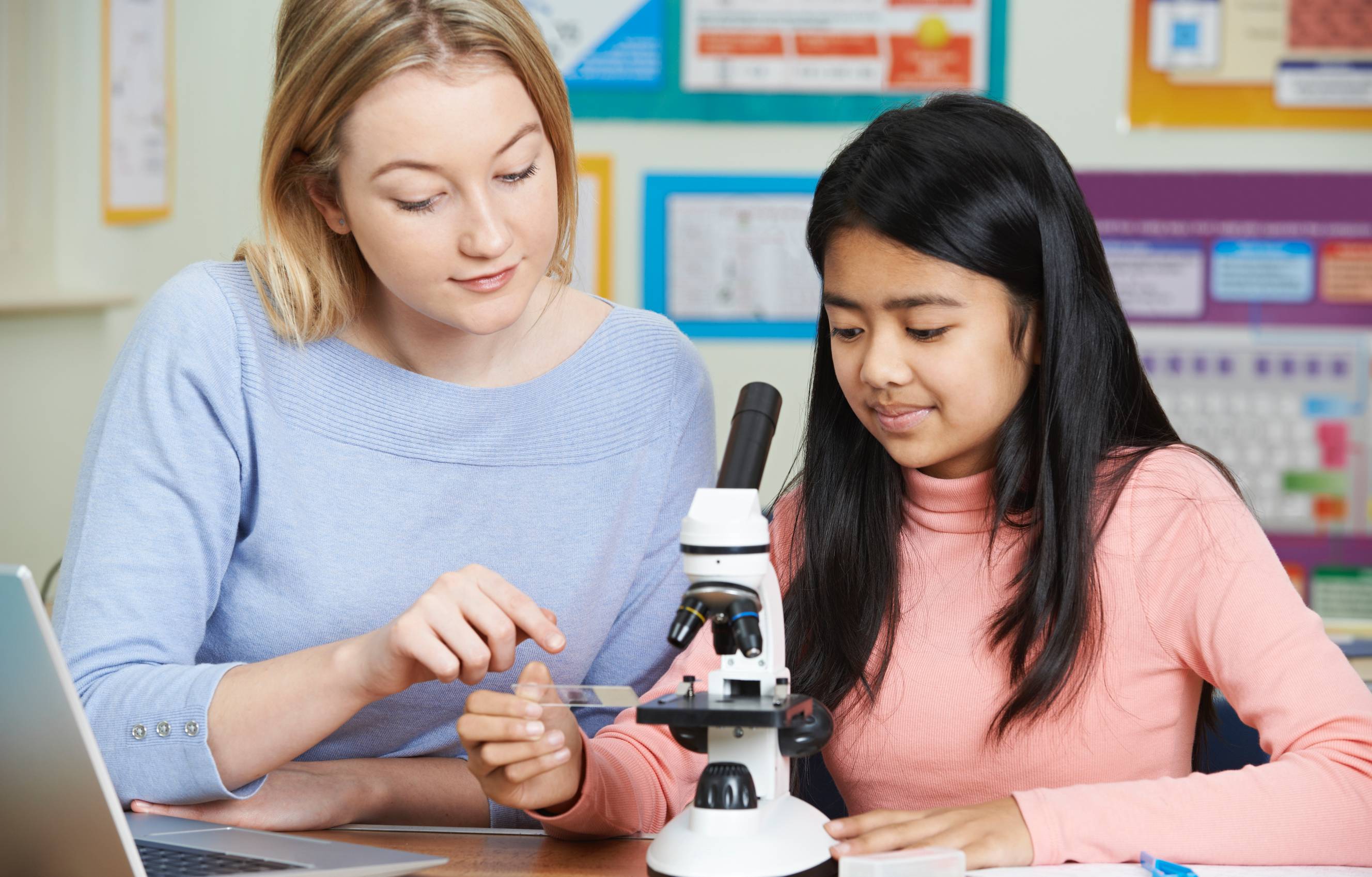 A biology tutor teaching a young girl with a microscope for their biology lesson.