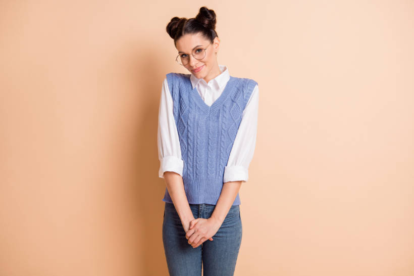 Alt text: Waistcoat vs Vest - Young woman wearing a pastel blue sweater vest over a white shirt