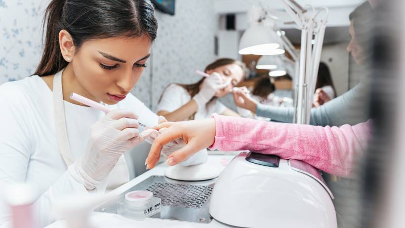 A nail technician diligently painting the nails of a customer's hand in a well-lit nail salon. - nail technician vs manicurist