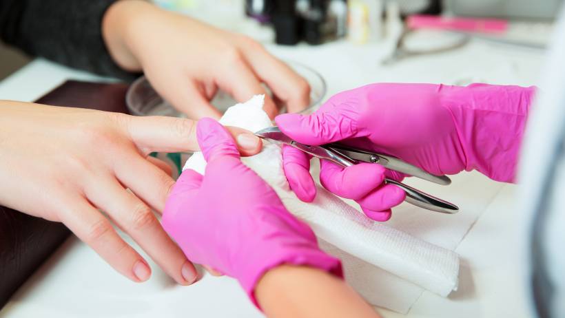 Hands of a nail technician carrying out a manicure procedure using specialised tools. - nail technician vs manicurist