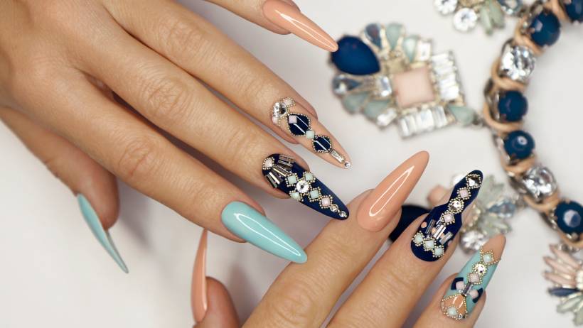 Hands with elaborately designed and decorated nails, featuring complex geometric patterns, rhinestones, and contrasting colours. - nail technician vs manicurist