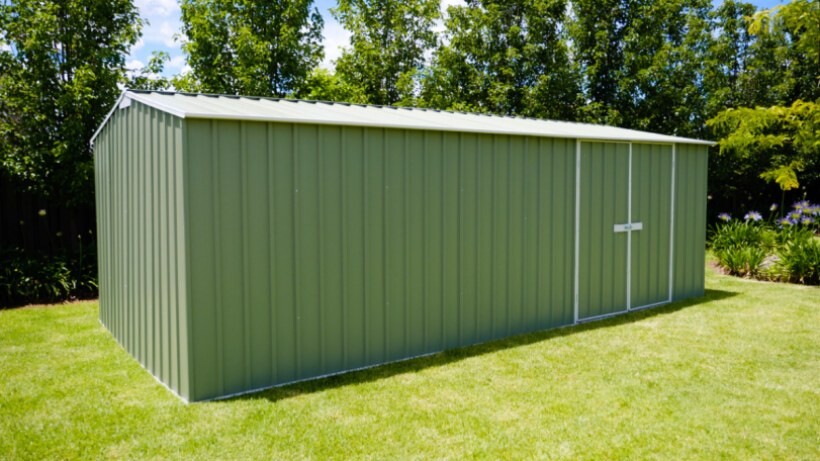 A green metal workshop shed from EasyShed set in a well-maintained backyard, surrounded by greenery and blue skies