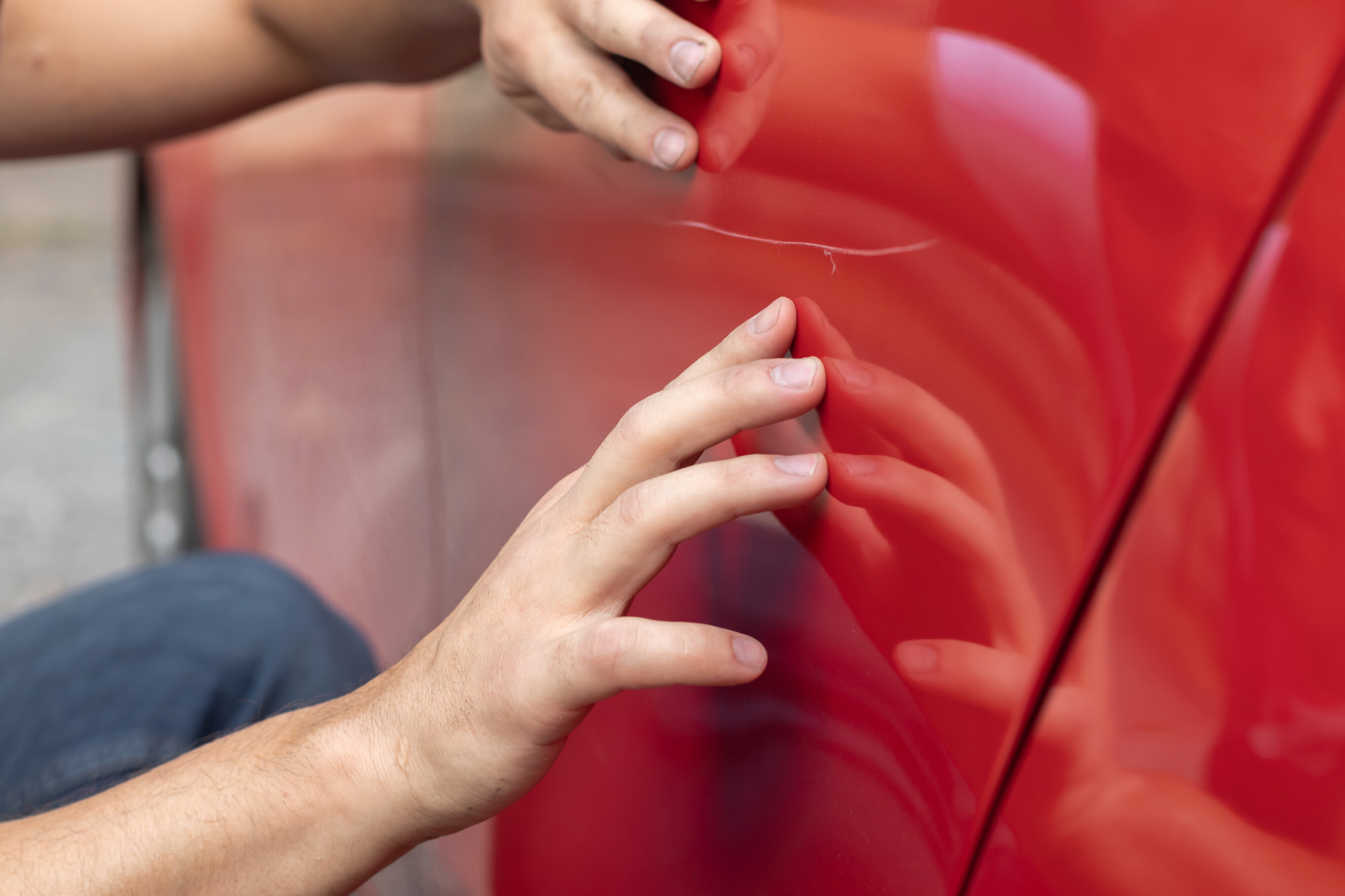 Close-up of a car scratch repair expert inspecting a scratch on a red vehicle, highlighting professional car scratch repair services near you.