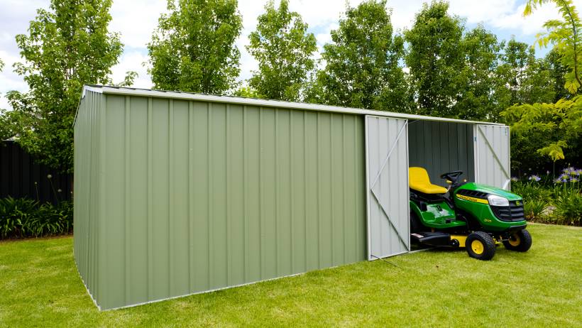 Green metal shed housing a lawn tractor in a grassy backyard - barn vs shed