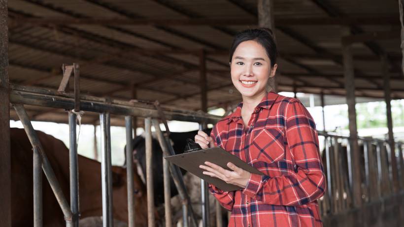 A woman in a plaid shirt smiling while holding a clipboard in a rustic barn setting - barn vs shed