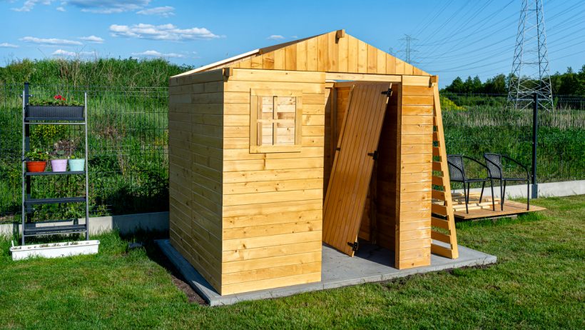 Timber frame shed vs steel shed - A timber frame shed under construction, featuring natural wood panels, a small window, and a door leaning against the structure