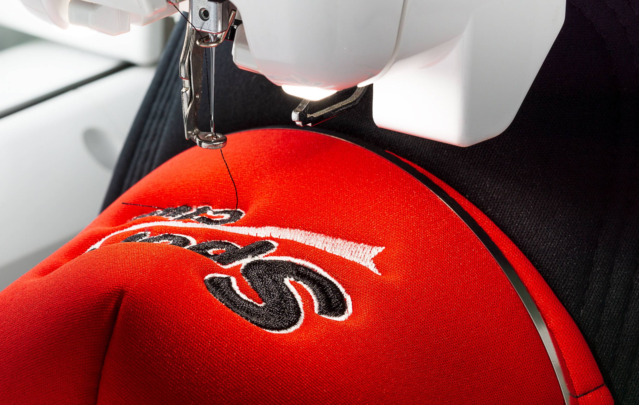 Close-up image of an embroidery service using a machine for a red and black sports cap.