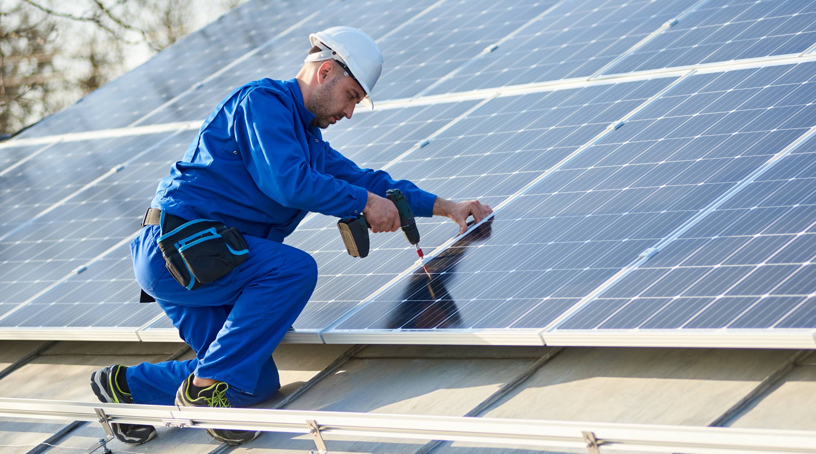 A professional technician wearing a protective blue suit and working on solar panel repairs on top of a modern home.