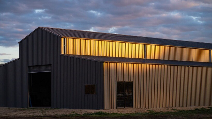 Barn vs shed - A large steel barn by Easyshed illuminated by golden sunlight, showcasing its spacious structure with high ceilings and multiple access points