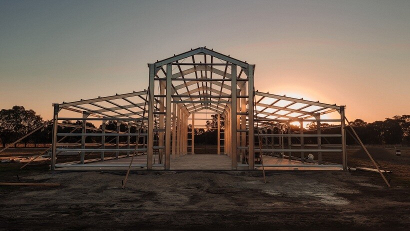 Barn vs shed - A steel barn frame under construction by Easyshed, set against a stunning sunset backdrop