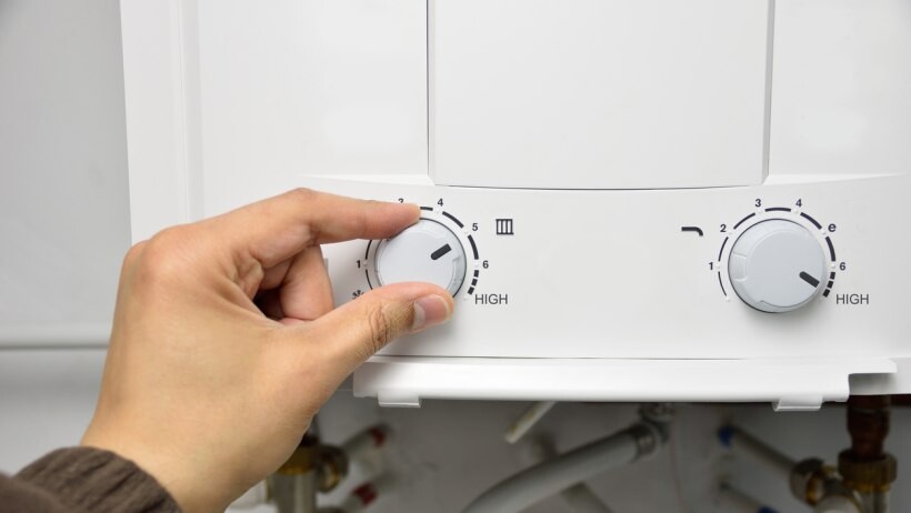 Electric boiler vs gas boiler - A person’s hand adjusting the control knob on a white boiler to increase the temperature